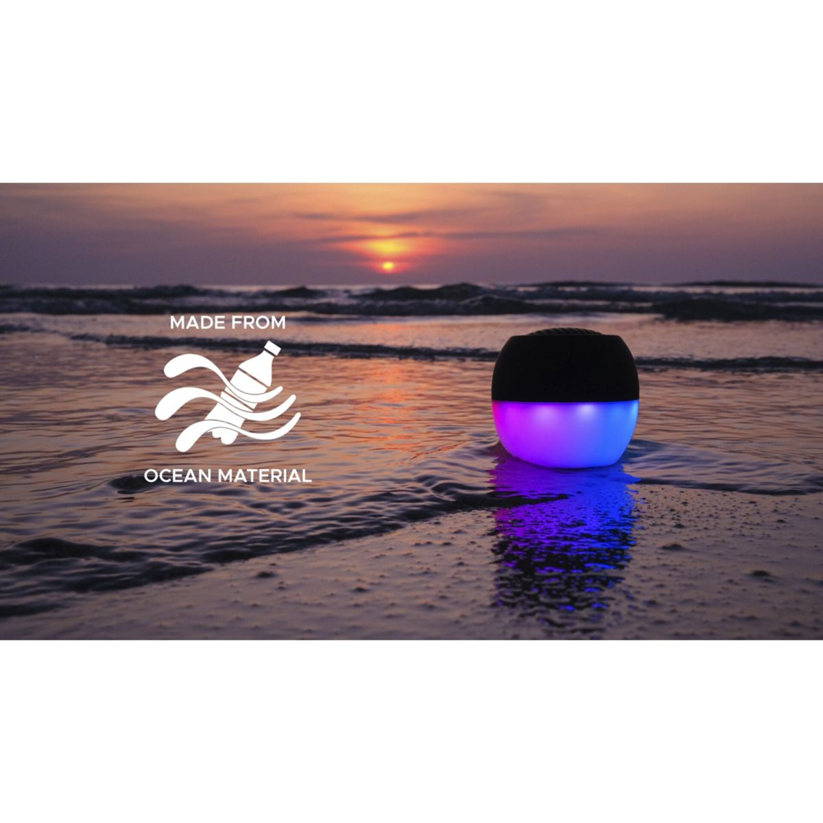 Głośnik na plaży z falami. Głośnik jest czarny i ma niebieskie/fioletowe światła. Tekst mówi 'wykonane z materiału oceanicznego'.