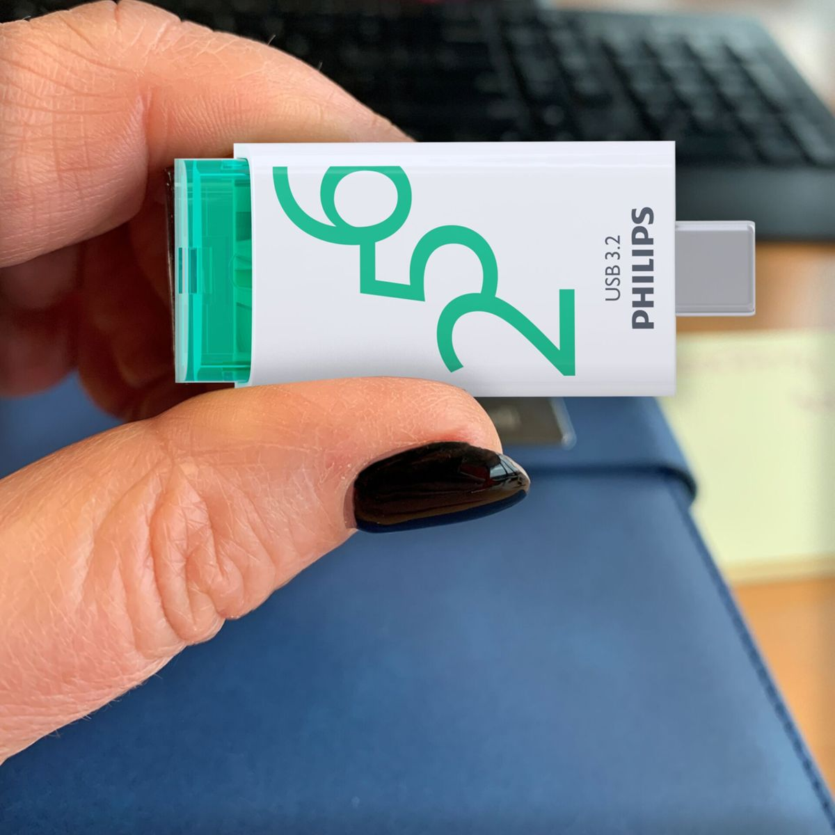 Osoba trzymająca pendrive z tekstem '256' i 'PHILIPS'. Dysk jest zielony i biały.