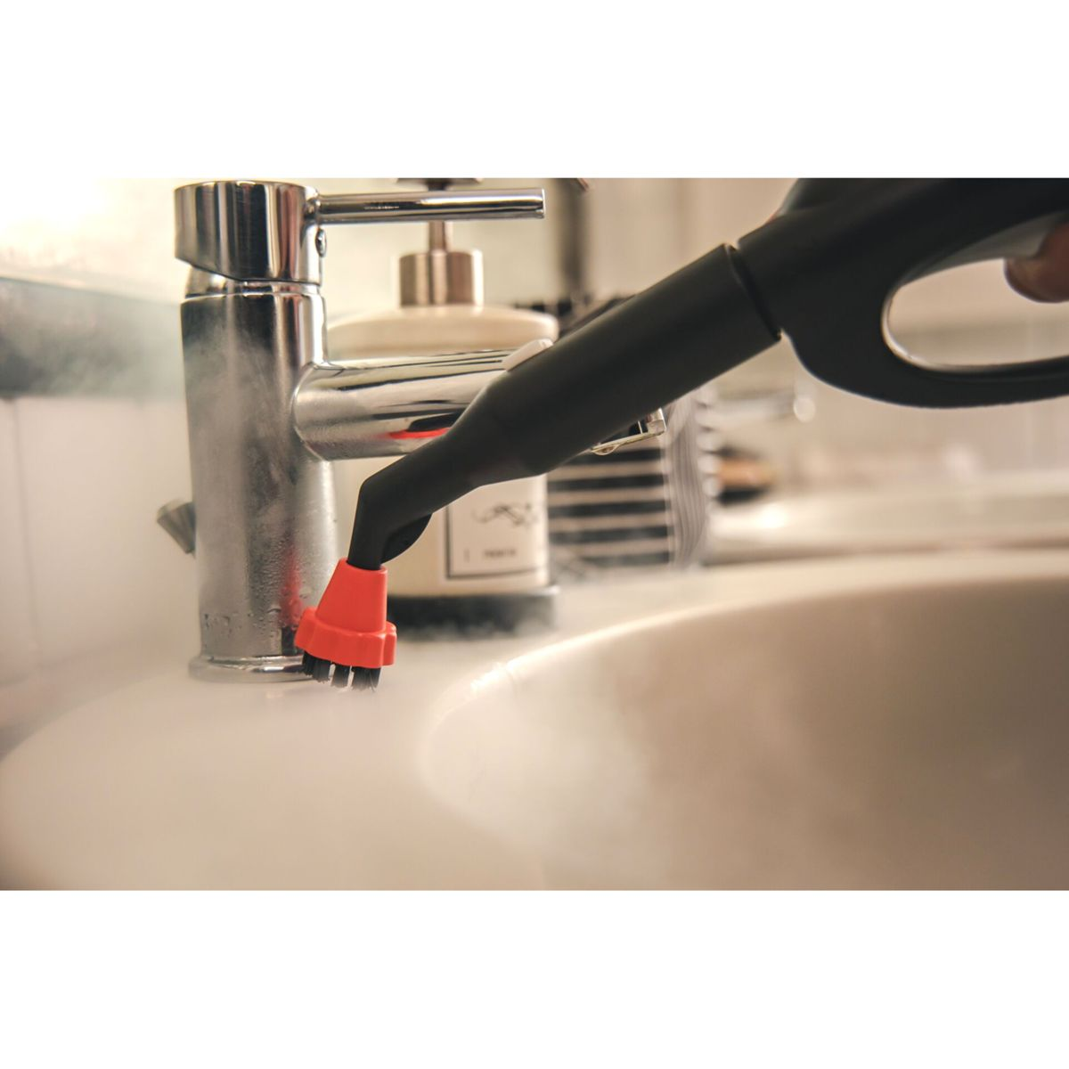 Głowica parownicy czyszcząca kran. Czarny uchwyt, pomarańczowa dysza. Biała umywalka i kran.