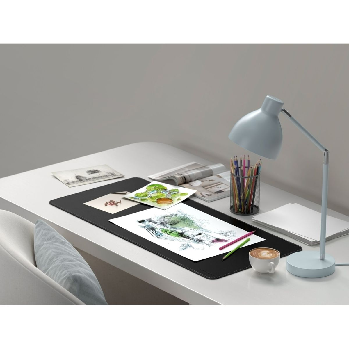 Una scrivania con forniture per il disegno, una lampada e una tazza di caffè. Ci sono disegni, penne e una lampada.