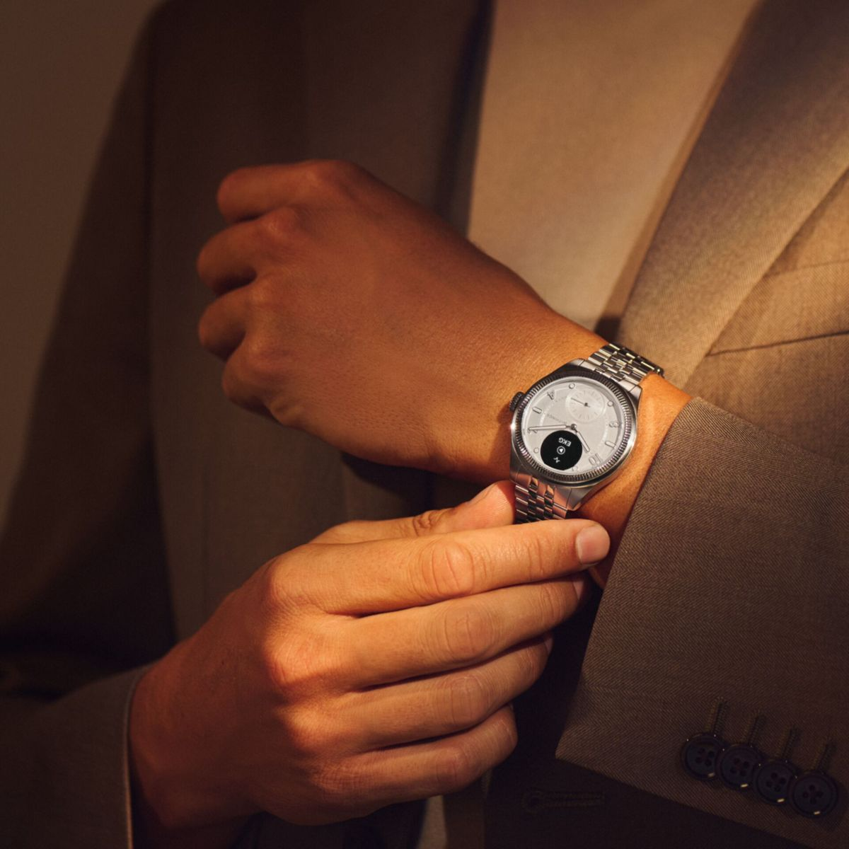 Mężczyzna noszący srebrny smartwatch z metalową bransoletą, pozujący w brązowym garniturze.