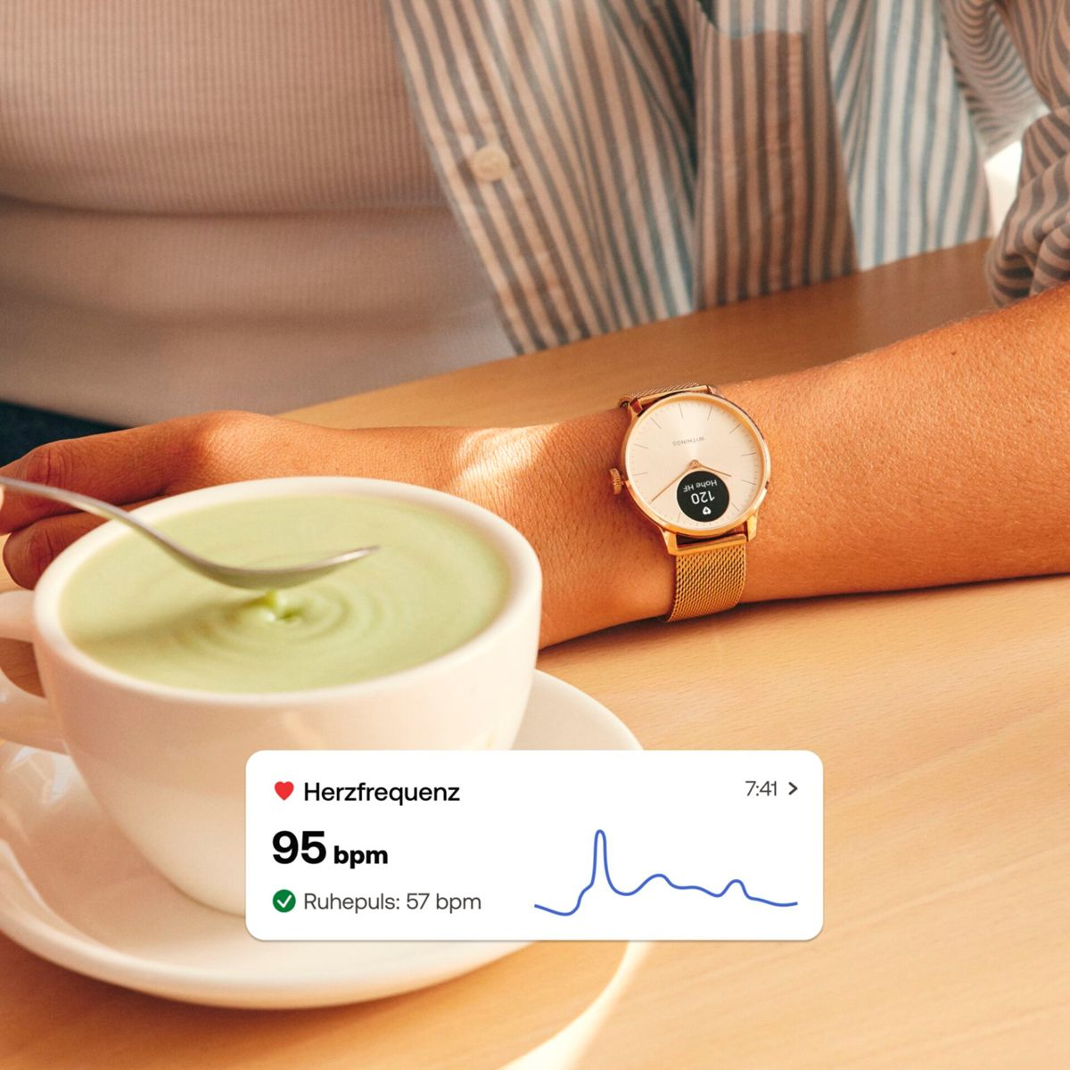 Osoba nosząca zegarek z danymi zdrowotnymi patrzy na filiżankę zielonego napoju z łyżeczką, z wykresem zdrowia.