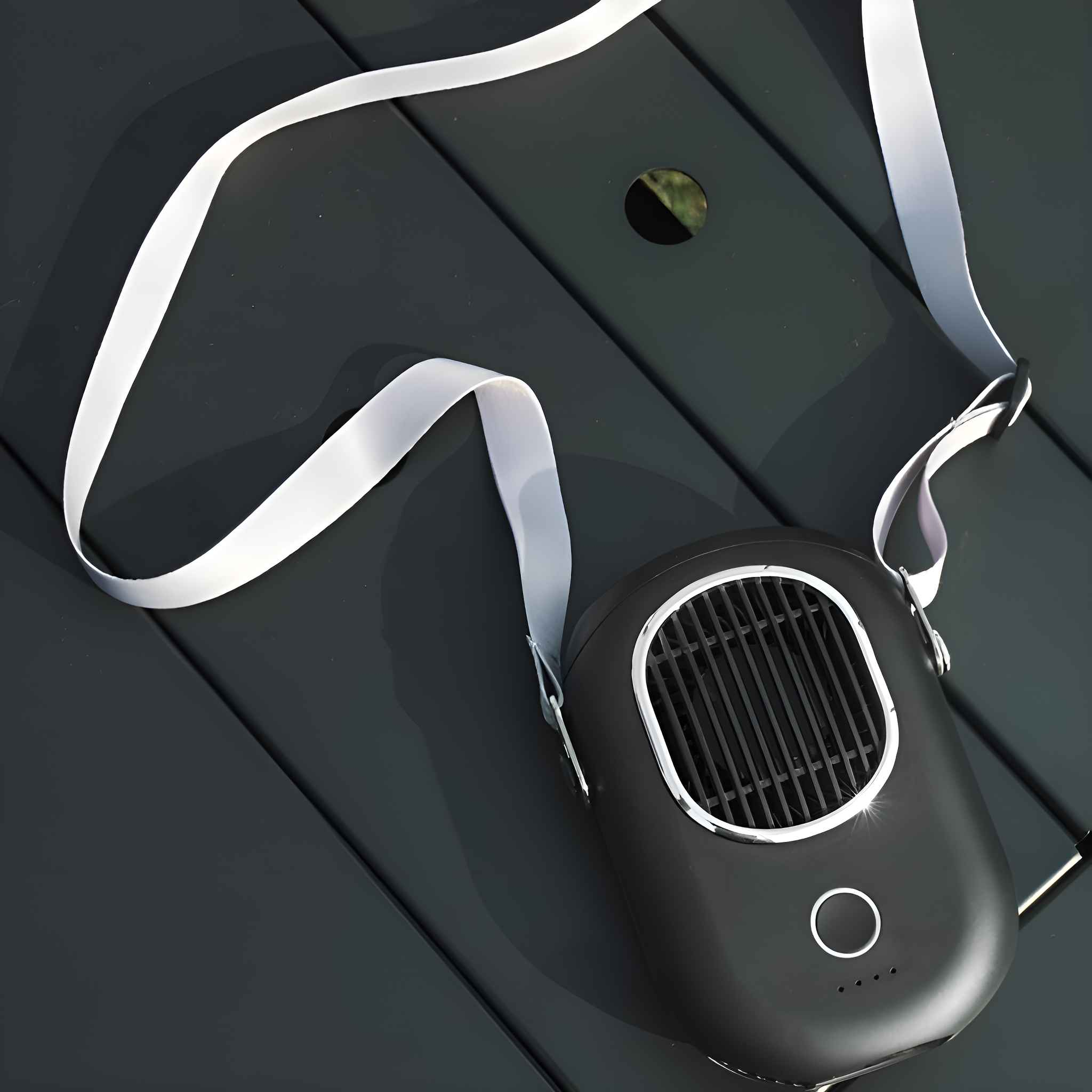 Schwarzer, ovaler persönlicher Ventilator mit weißem Riemen. Er liegt auf einem dunkelgrauen Tisch.