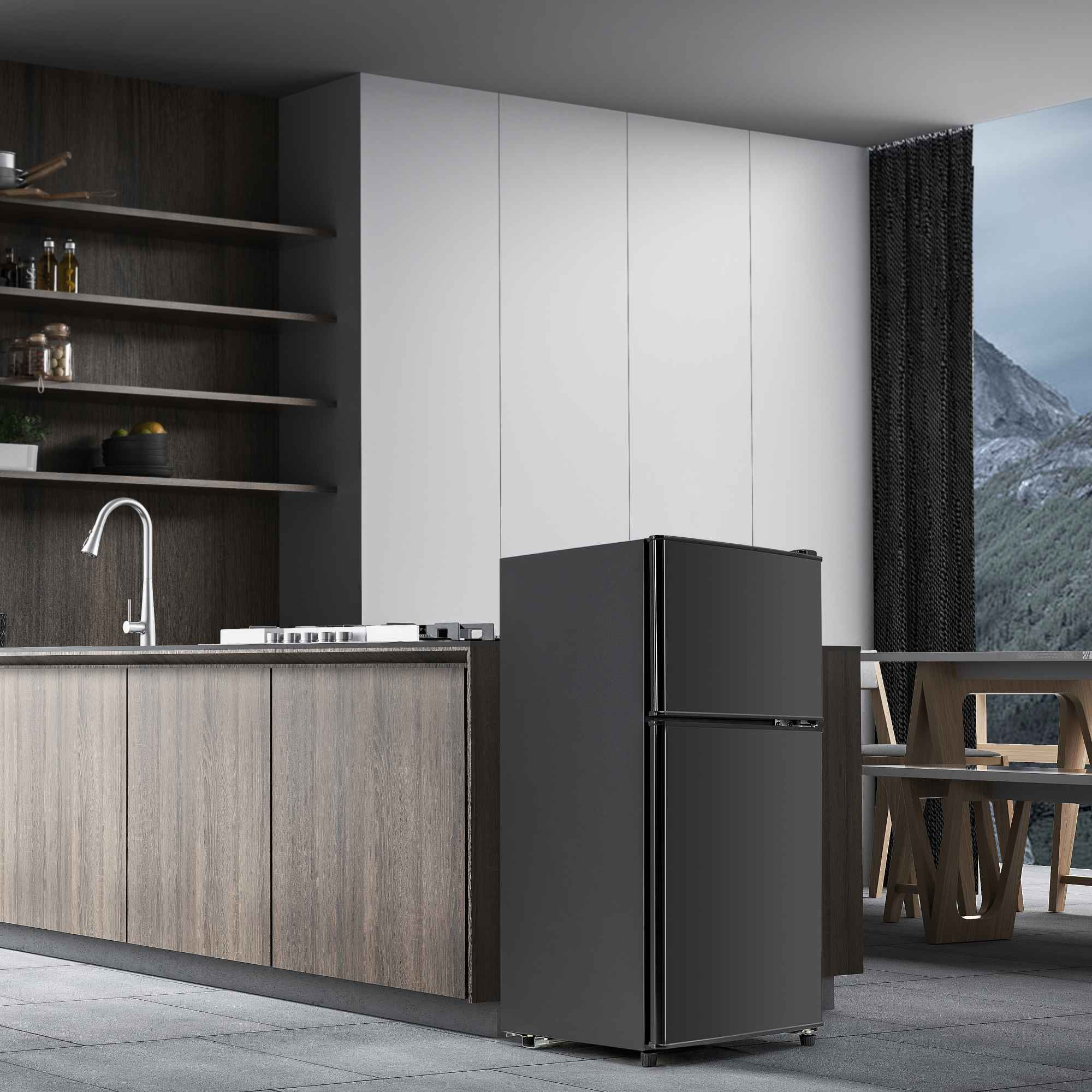 Ein schwarzer Kühlschrank steht in einer Küche. Holzschränke, ein Waschbecken und ein Fenster mit Bergblick sind sichtbar.