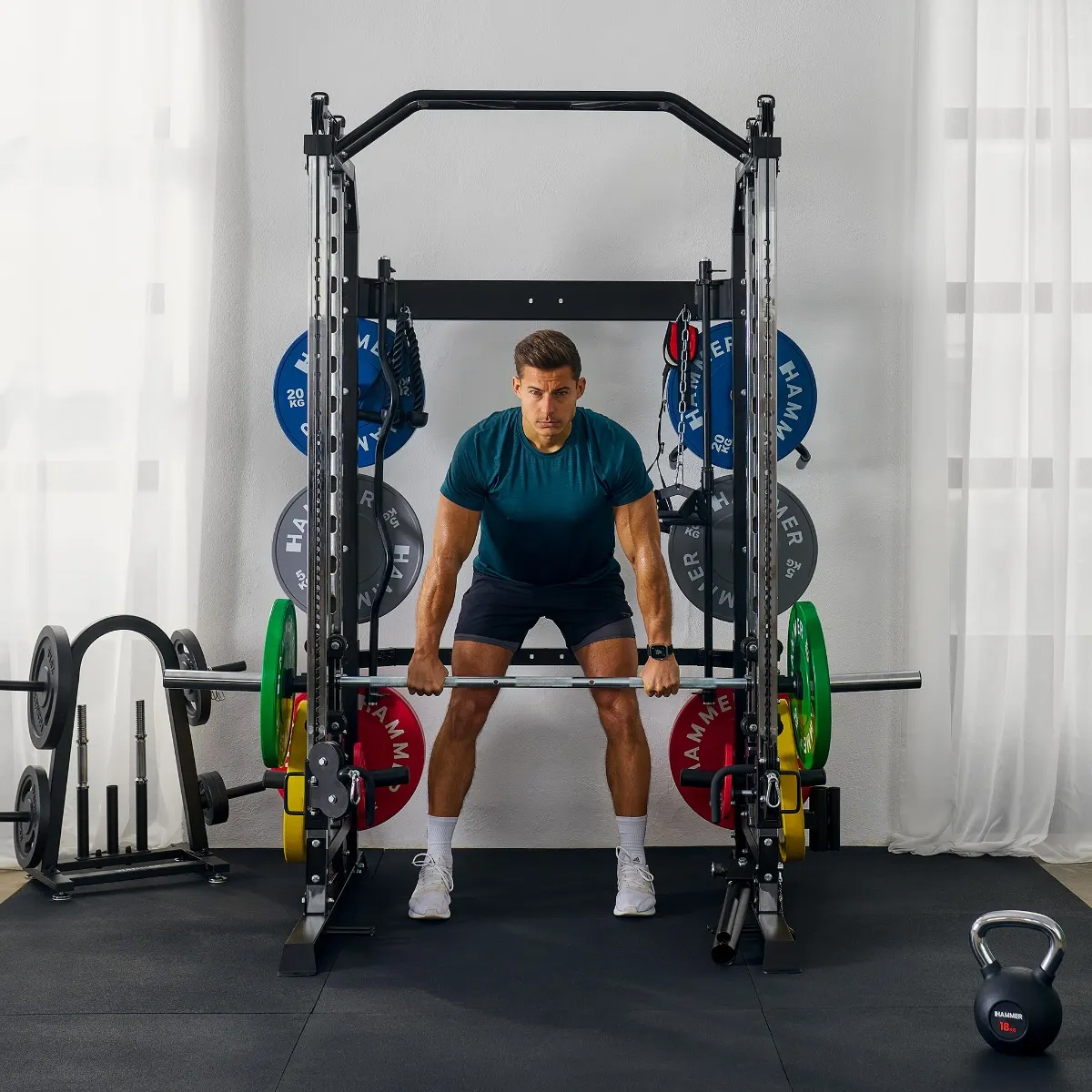 Ein Mann hebt Gewichte in einem Fitnessstudio. Er trägt ein blaues Hemd und Shorts. Eine Kettlebell liegt auf dem Boden.