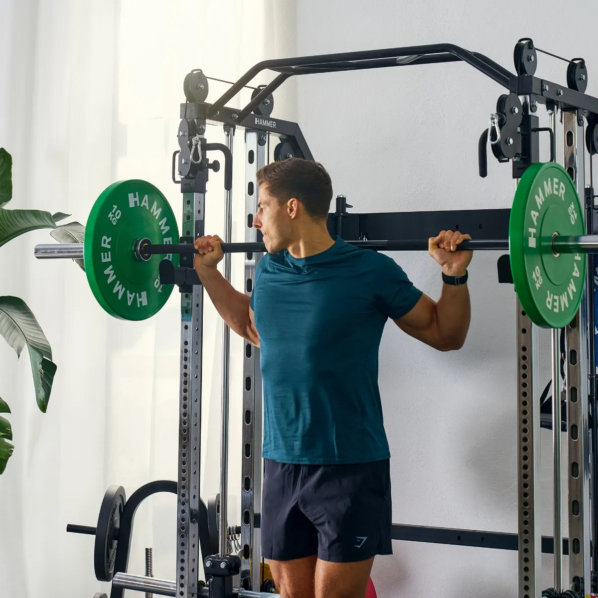 Ein Mann hebt Gewichte in einem Fitnessstudio mit einer Maschine. Grüne Gewichte sind an den Seiten. Er trägt ein blaues Hemd.