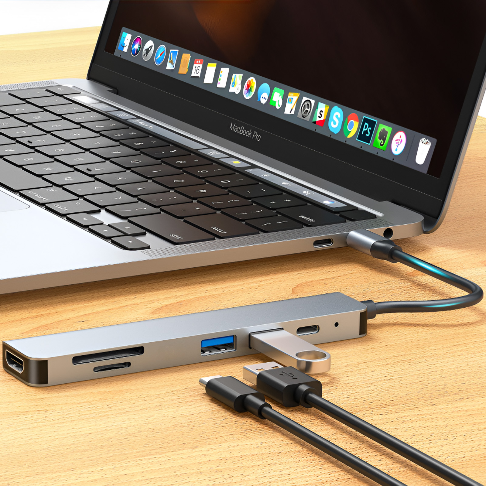 Ein Laptop, der mit einem silbernen Hub mit mehreren Anschlüssen verbunden ist. Kabel und ein USB-Laufwerk sind ebenfalls sichtbar.
