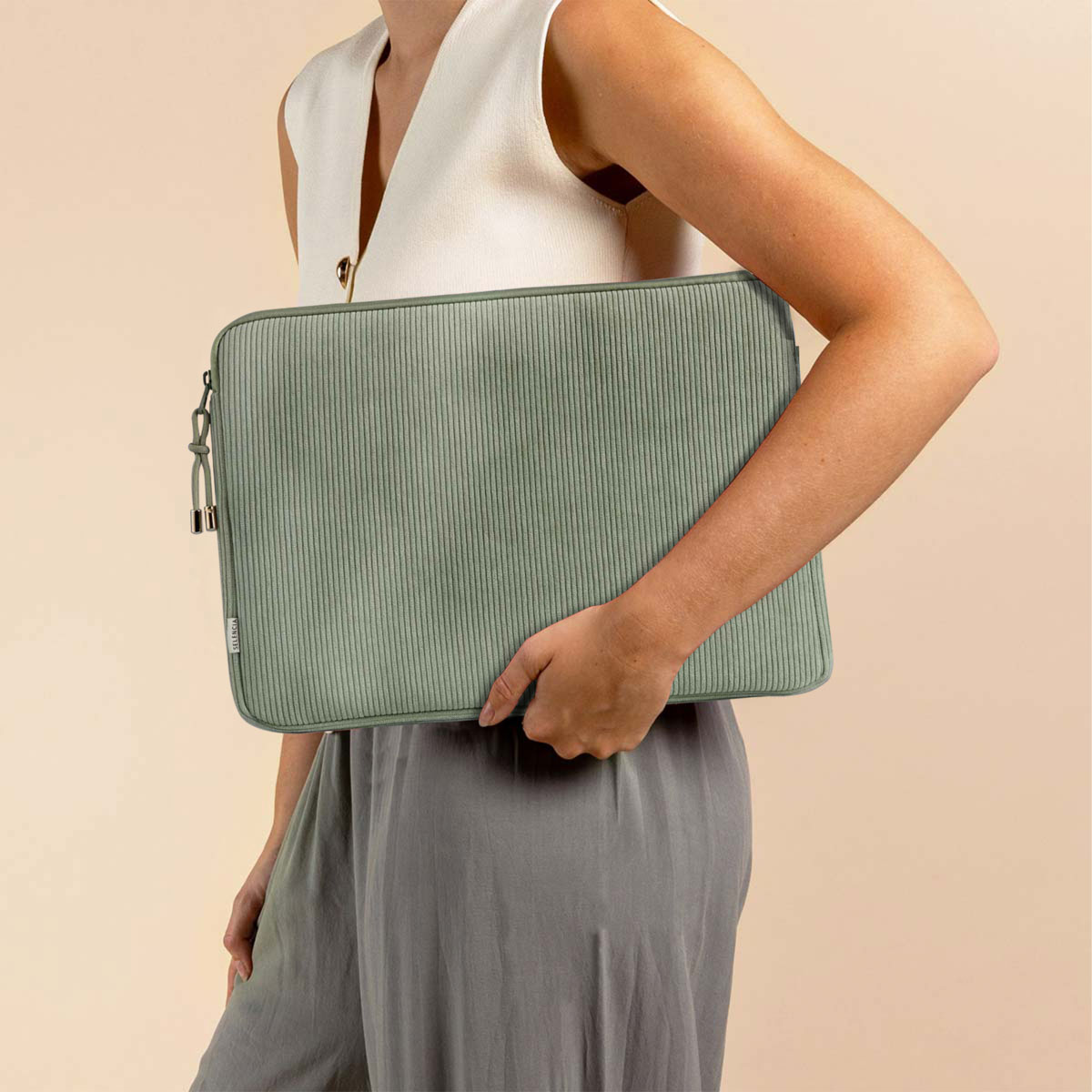 A woman holding a green corduroy laptop sleeve. The background is a beige wall.
