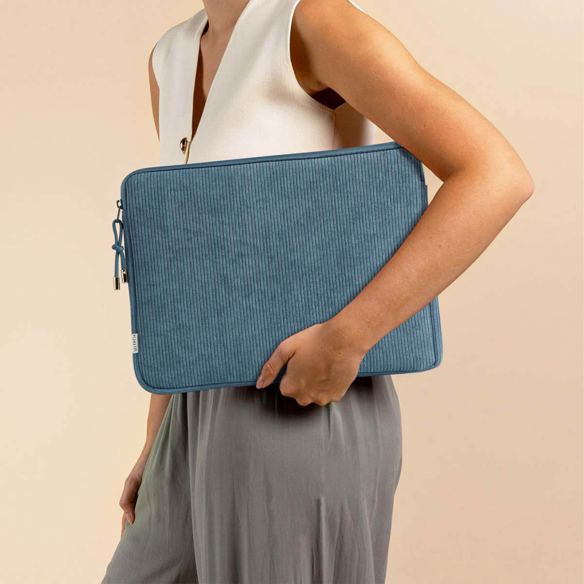 A woman holds a blue laptop sleeve. The sleeve has a zipper and is made of corduroy material.
