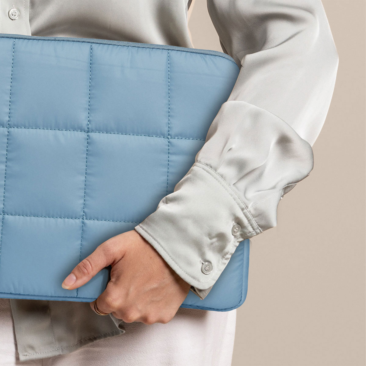 Een persoon die een lichtblauwe, gewatteerde laptophoes vasthoudt. De achtergrond is beige.