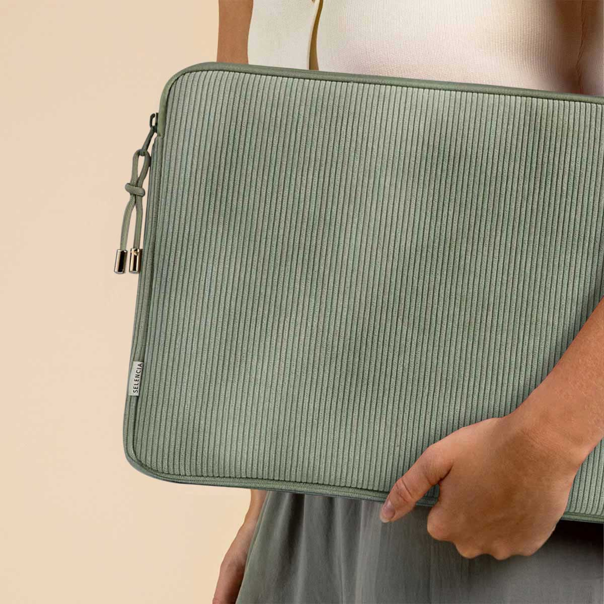 Person holding a green corduroy laptop case. The case has a zipper, and the brand SELENCIA is visible.