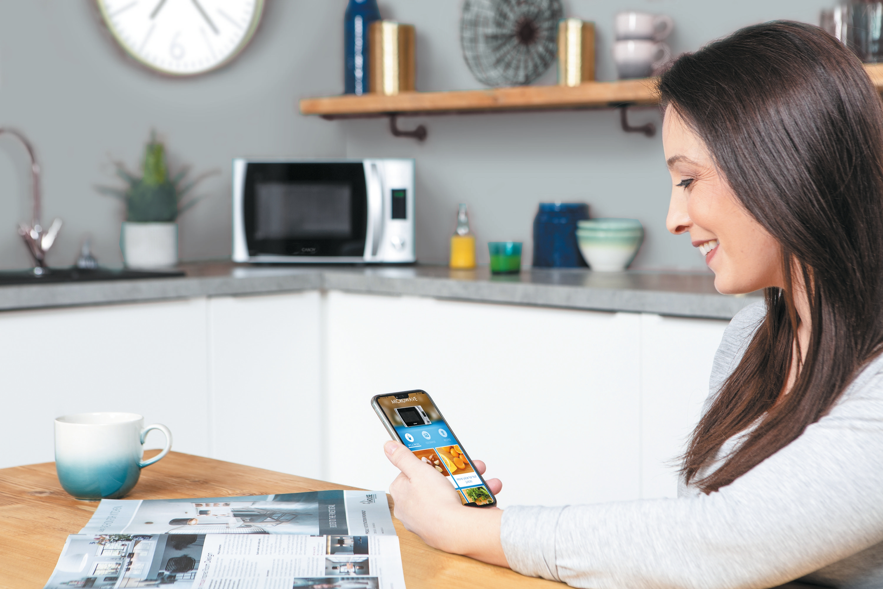Donna usa smartphone con app microonde in cucina con microonde sullo sfondo.