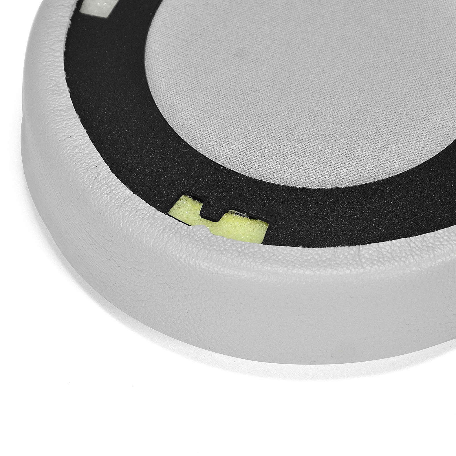 Zbliżenie jasnoszarej poduszki nausznej z czarnym wewnętrznym pierścieniem i żółtymi piankowymi wkładkami, na białej powierzchni.