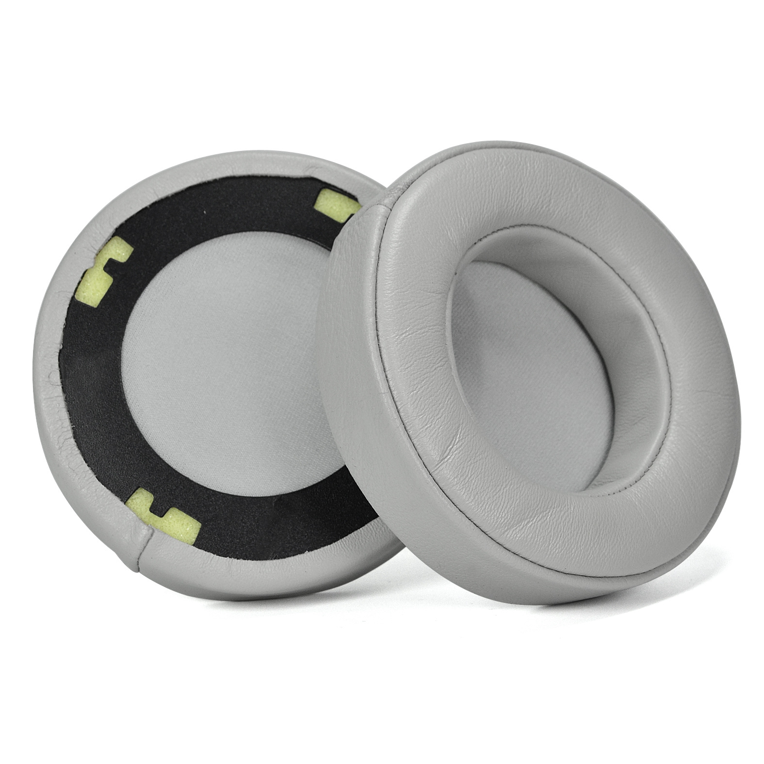 Dwie szare, okrągłe nauszniki do słuchawek, jedna pokazująca wnętrze, z czarną i żółtą pianką, na białym tle.
