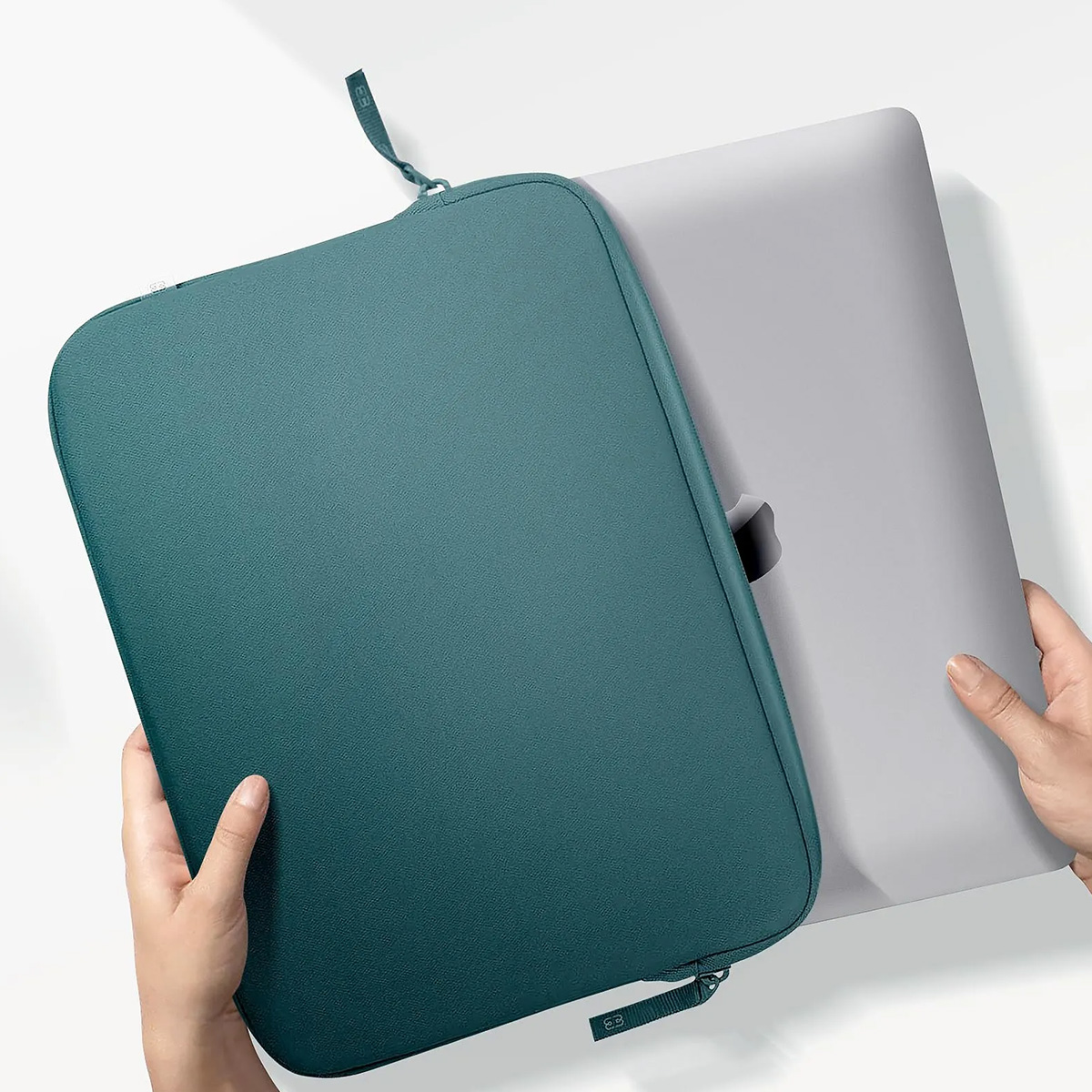 Une housse d'ordinateur portable turquoise avec un ordinateur portable à l'intérieur, tenue par deux mains.