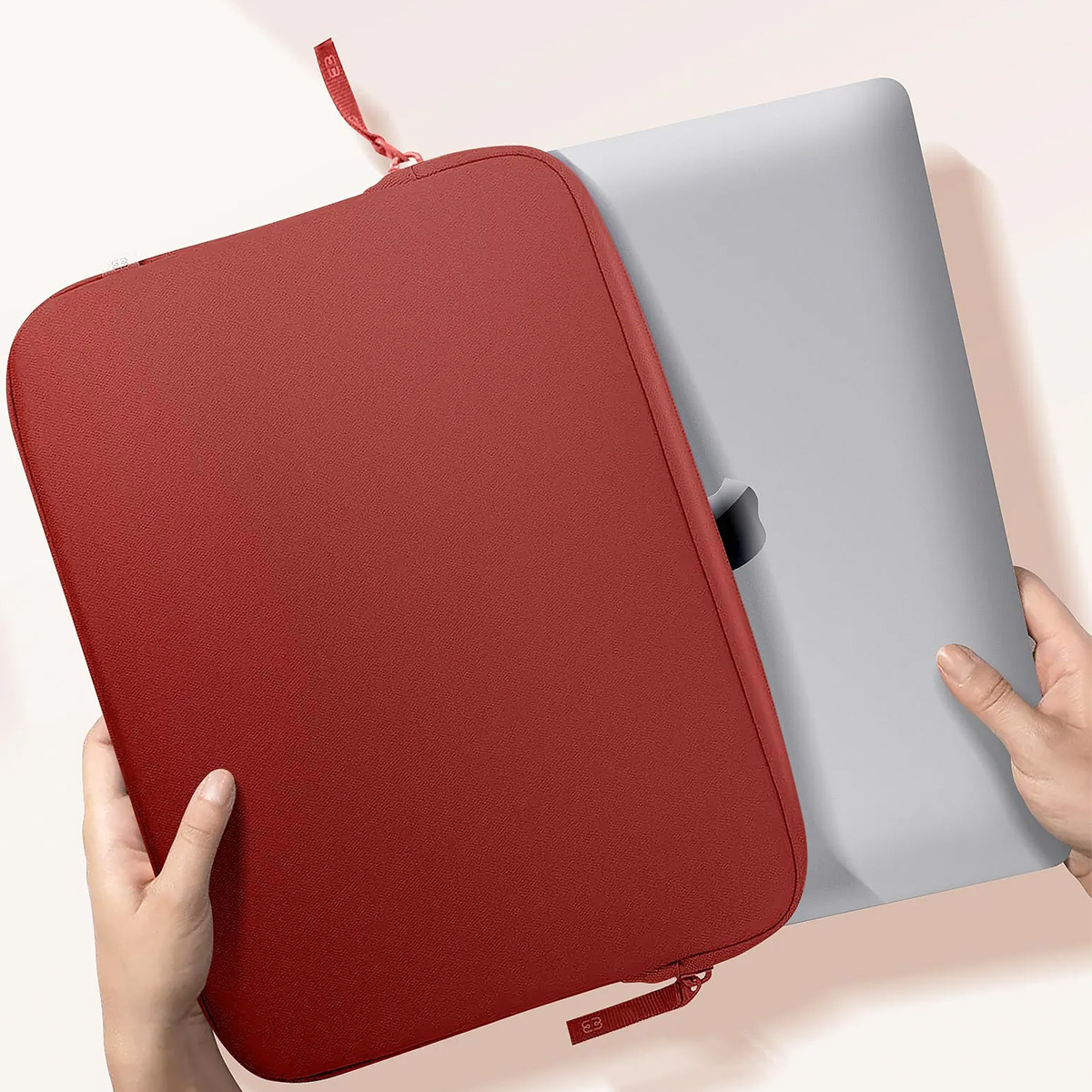 Une housse d'ordinateur portable rouge avec un ordinateur portable à l'intérieur, tenue par deux mains.