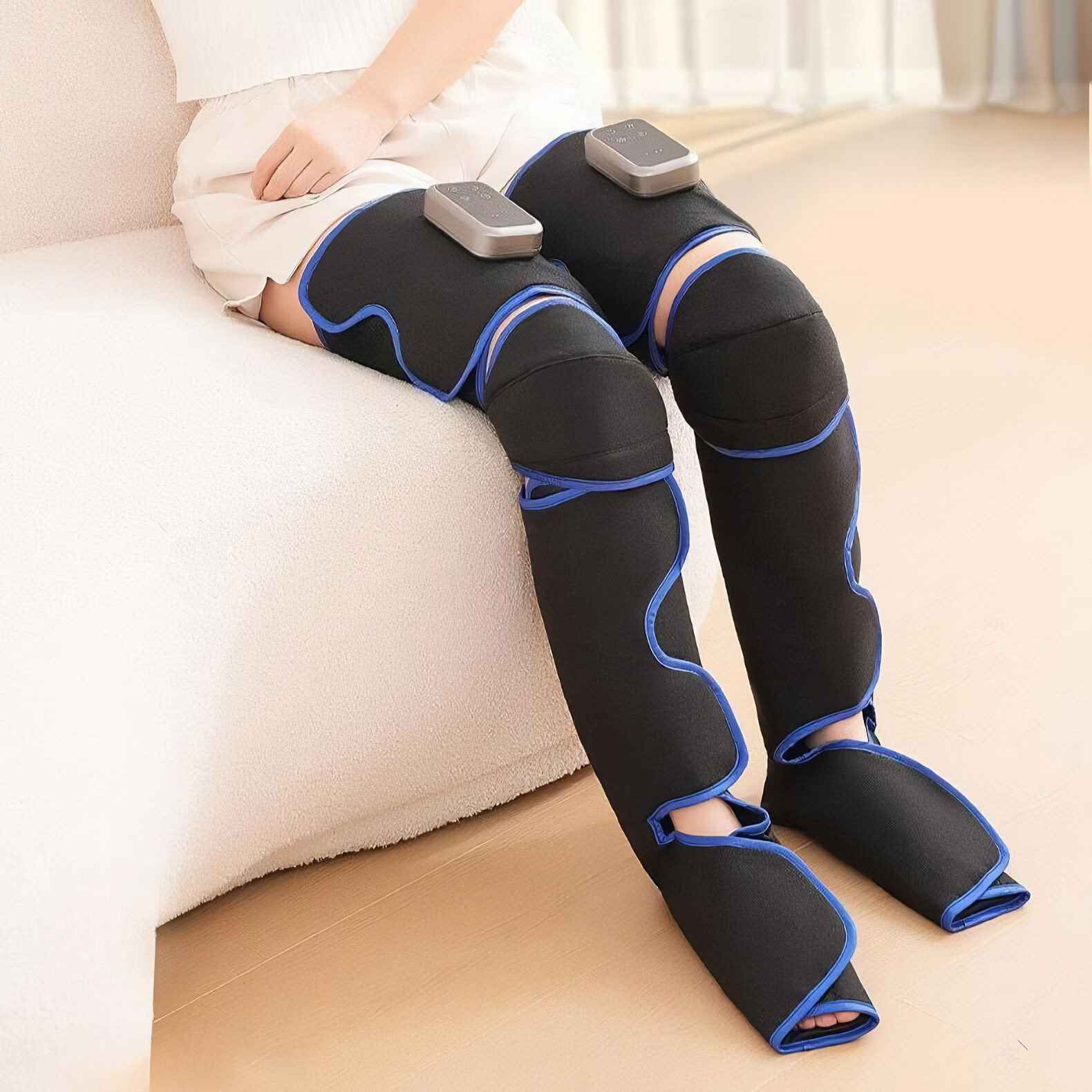 Eine Person sitzt mit Beinmassagegeräten an den Beinen. Die Massagegeräte sind schwarz mit blauem Rand.