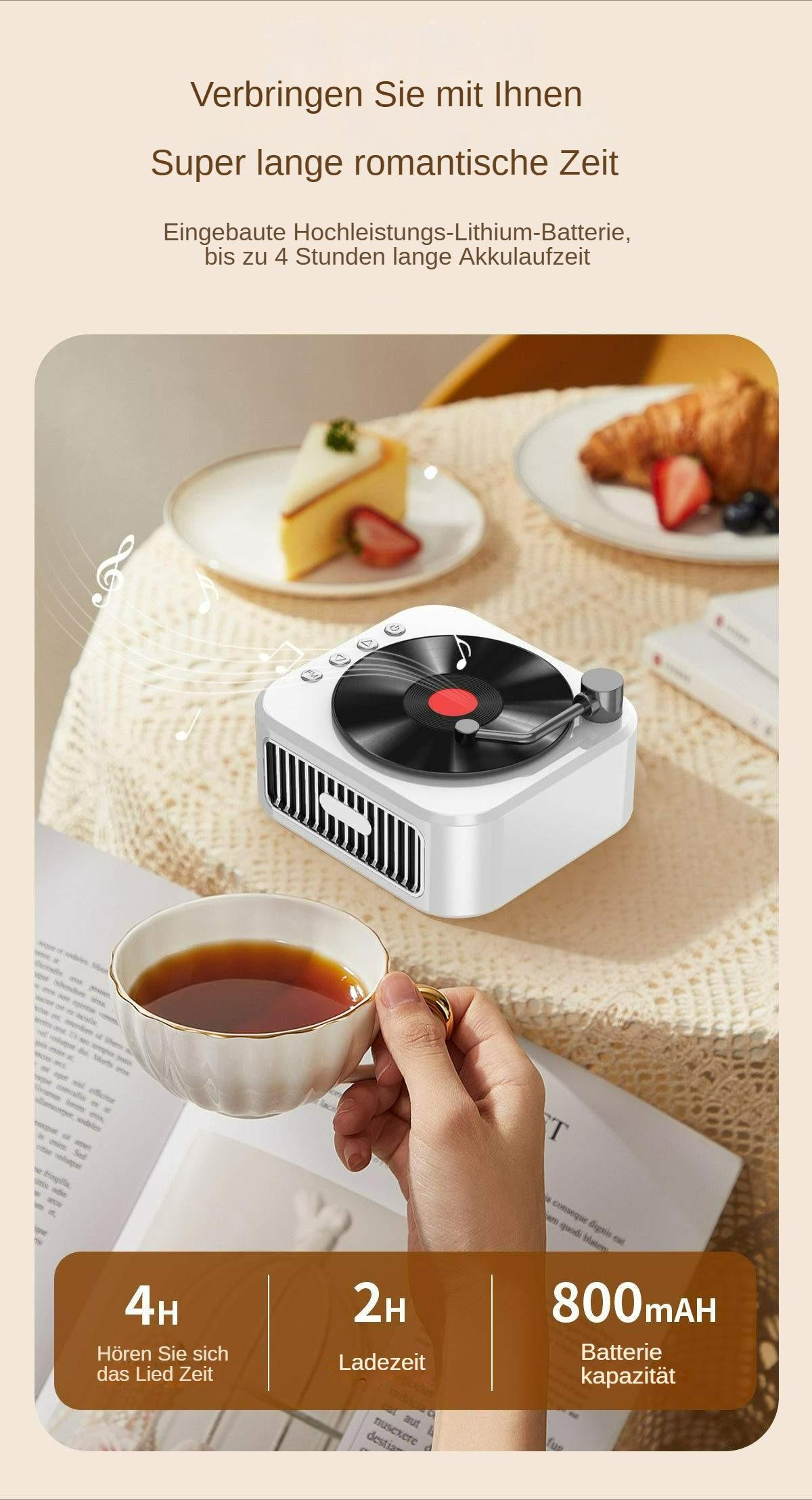 Eine Hand hält eine Tasse in der Nähe eines tragbaren Plattenspielers, mit Lebensmitteln wie Croissants und Beeren im Hintergrund.