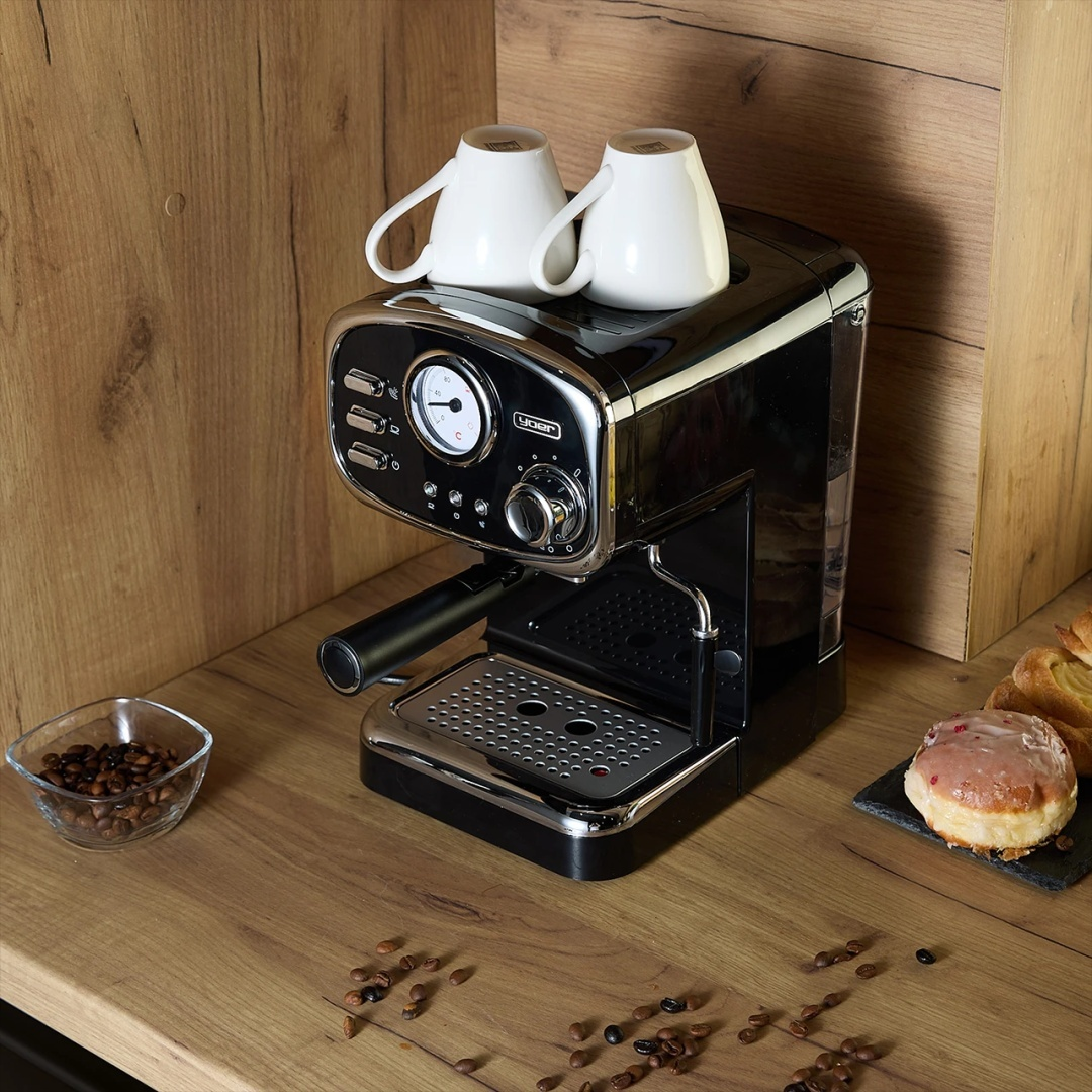 Czarny ekspres do kawy z filiżankami na drewnianym blacie z ziarnami kawy i ciastkami.