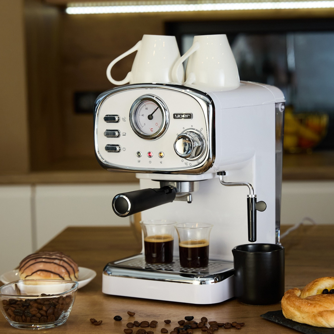 Biały ekspres do kawy z dwoma filiżankami na górze i dwiema szklankami kawy. Ziarna na stole.