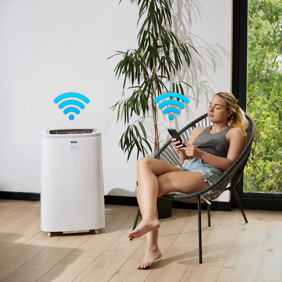 Kobieta korzystająca z telefonu, obok której stoi biały oczyszczacz powietrza.