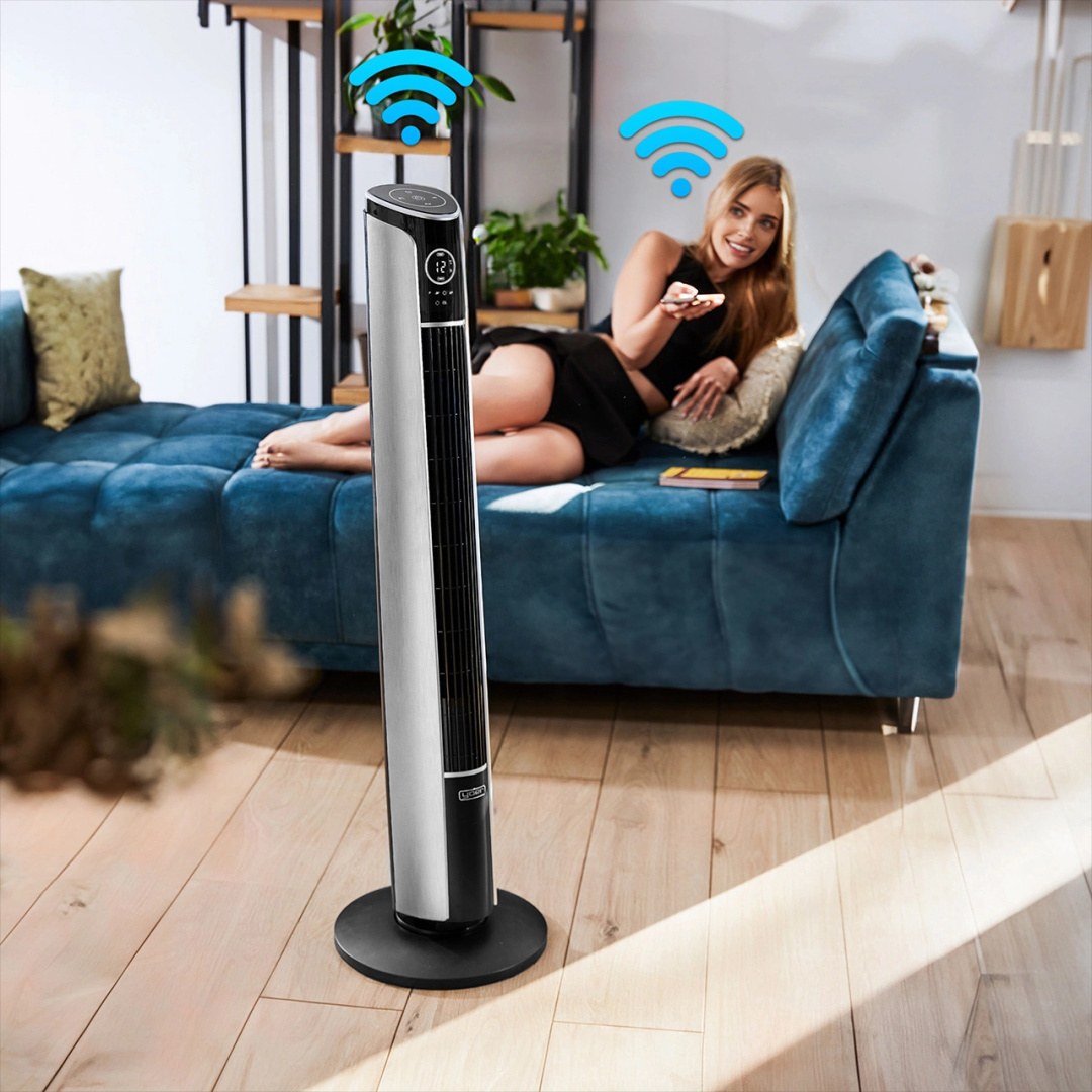 Kobieta używa aplikacji w telefonie do sterowania wentylatorem wieżowym. Inna kobieta siedzi na kanapie.