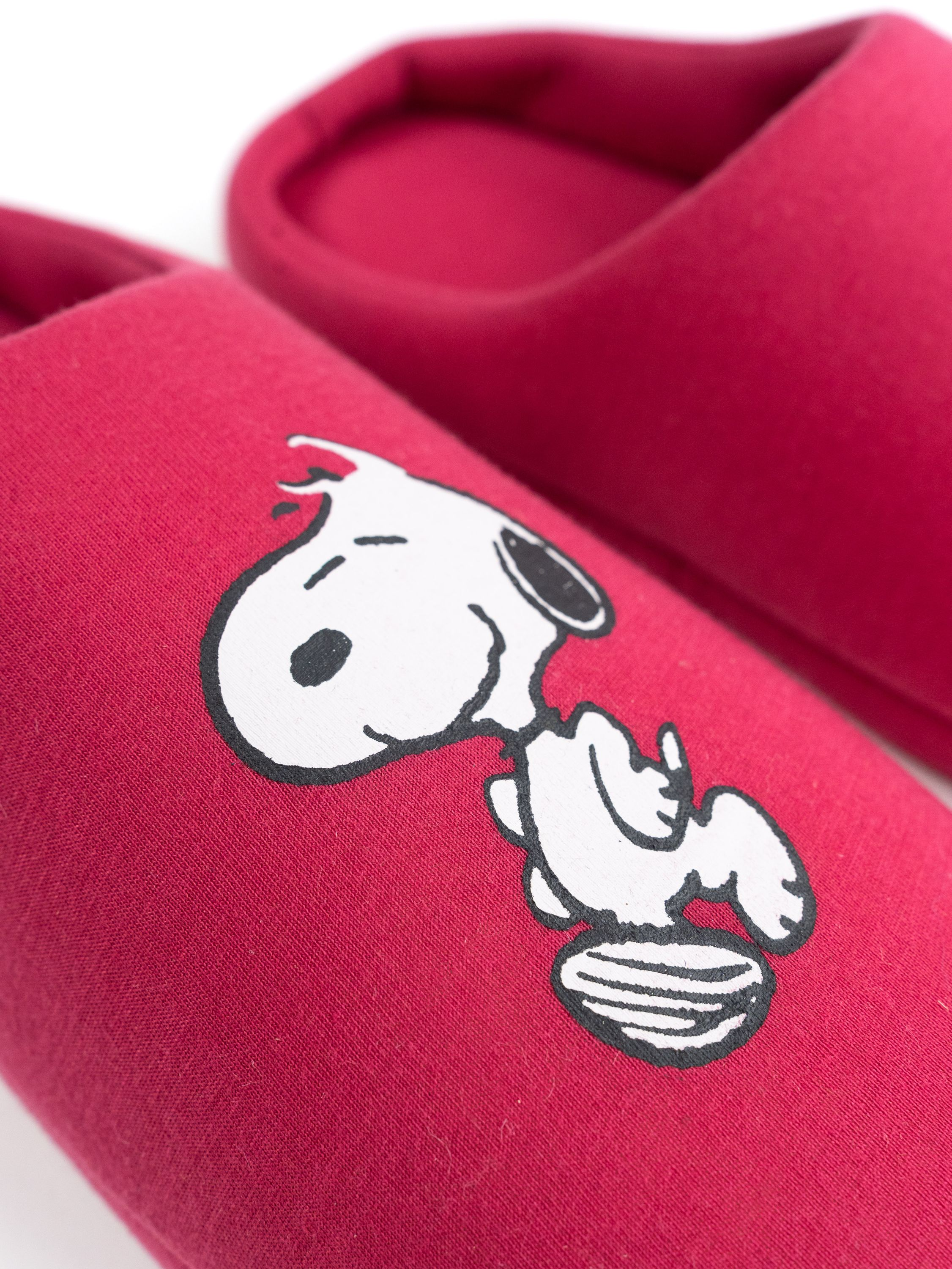 Nahaufnahme eines Snoopy-Hausschuhs. Rote Farbe. Snoopy's Gesicht ist auf dem Hausschuh. Weißer Hintergrund.