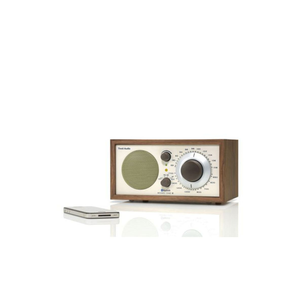 Ein Radio im Retro-Stil mit Holzrahmen. Es hat eine grüne Lautsprecherabdeckung, zwei Knöpfe und ein Zifferblatt. Ein silbernes Gerät liegt daneben.