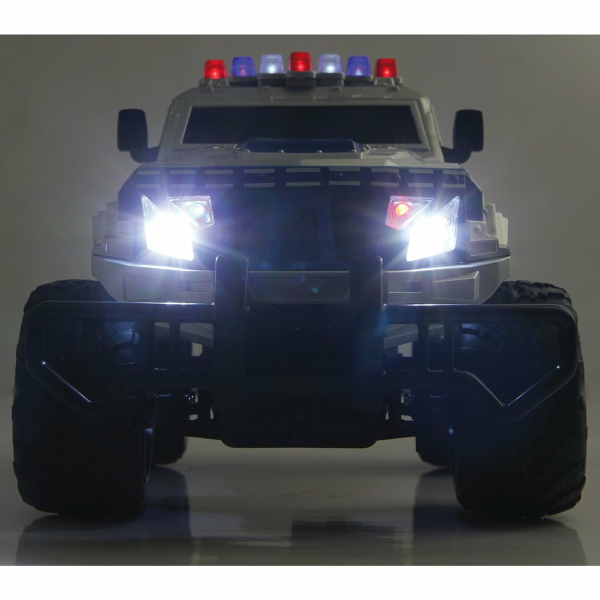 Vorderansicht eines silbernen Polizeiwagens mit hellen Scheinwerfern und roten/blauen Lichtern oben, mit großen schwarzen Reifen.