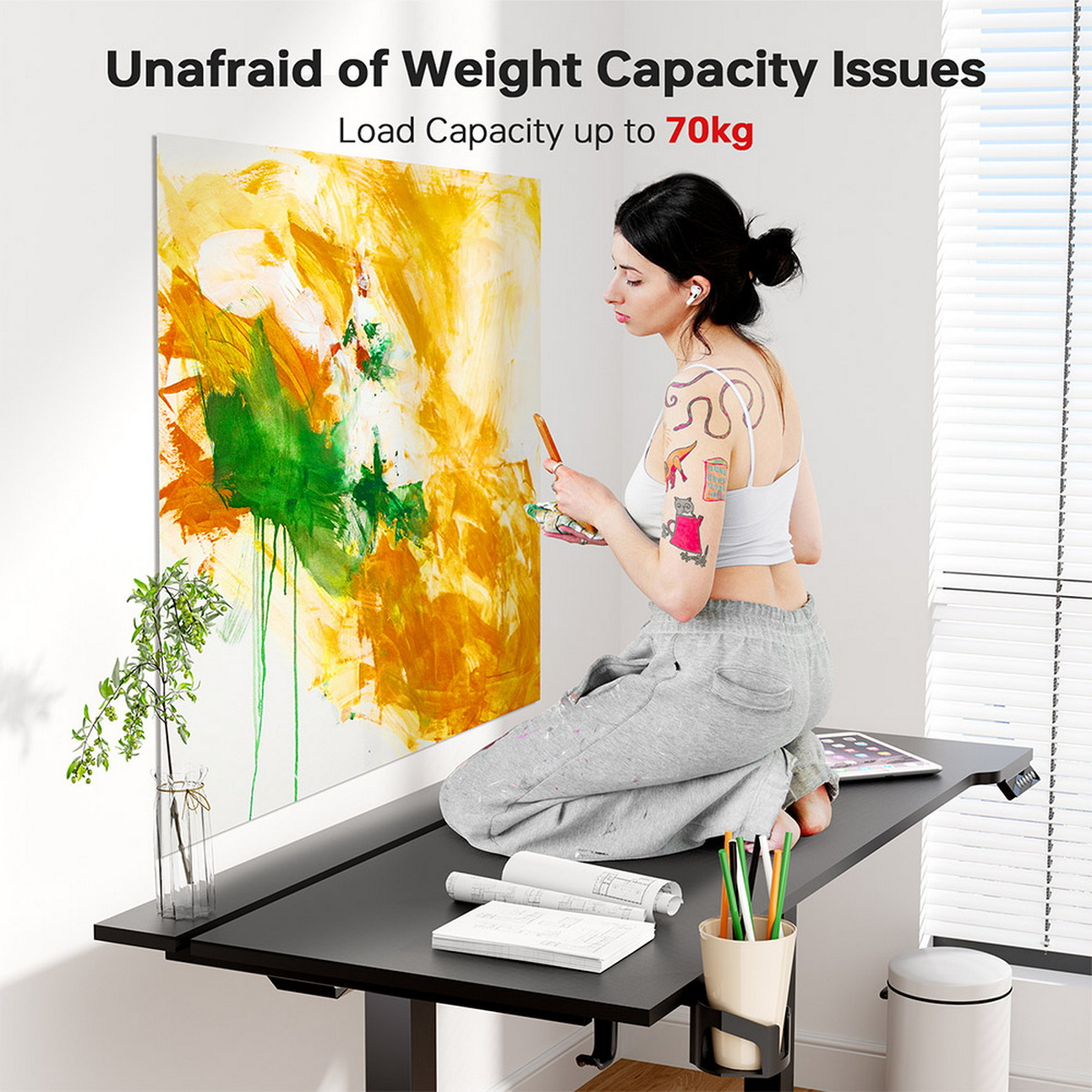 Kobieta siedzi przy biurku ze sztuką i ołówkami. Tekst mówi: Bez obaw o problemy z obciążeniem. Duży obraz na ścianie.