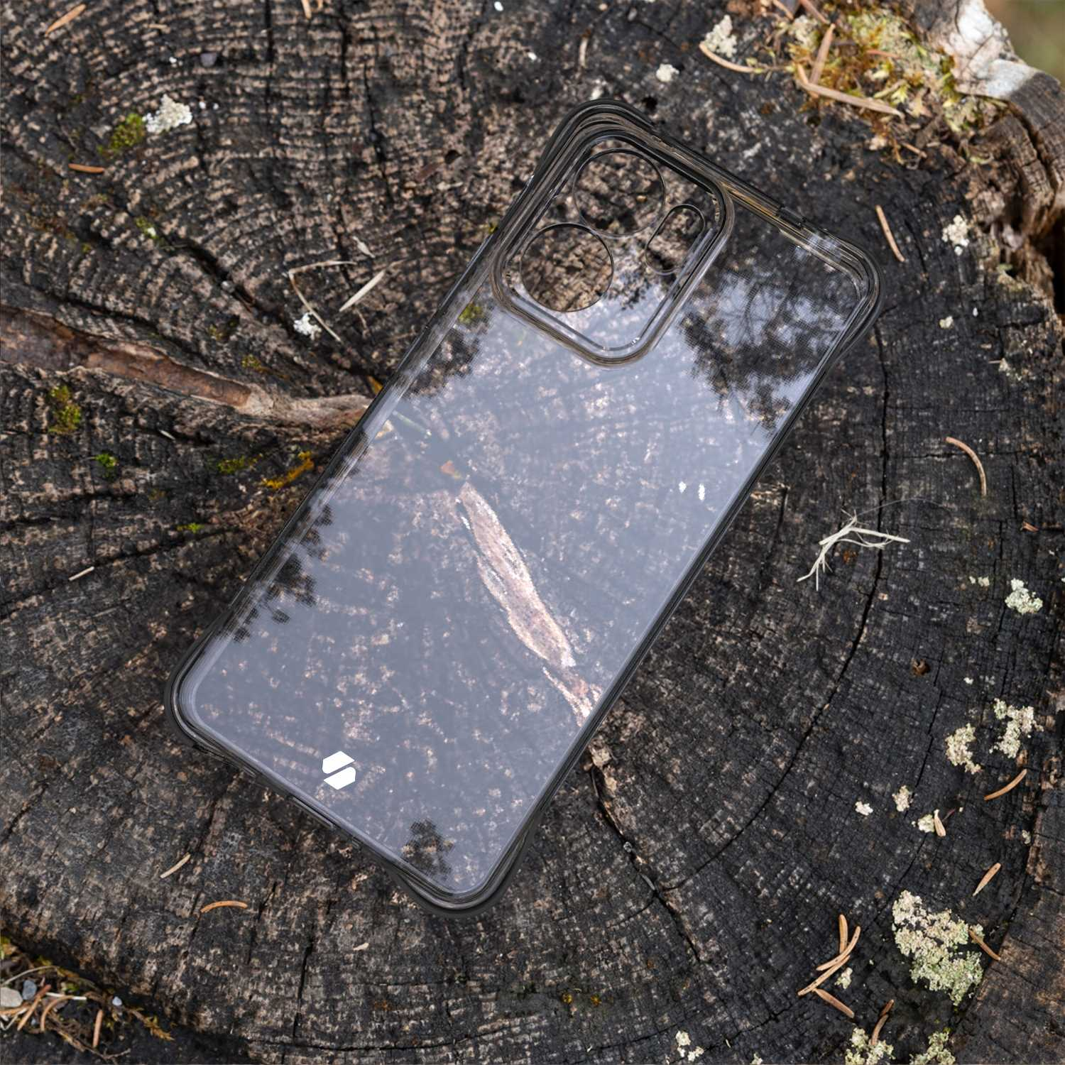 Przezroczyste etui na telefon na pniu drzewa. Przez etui widać słoje drewna.