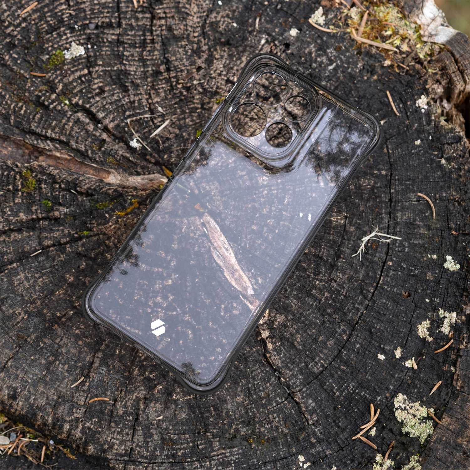 Przezroczyste etui na telefon na pniu drzewa. Przez etui widać słoje drewna.