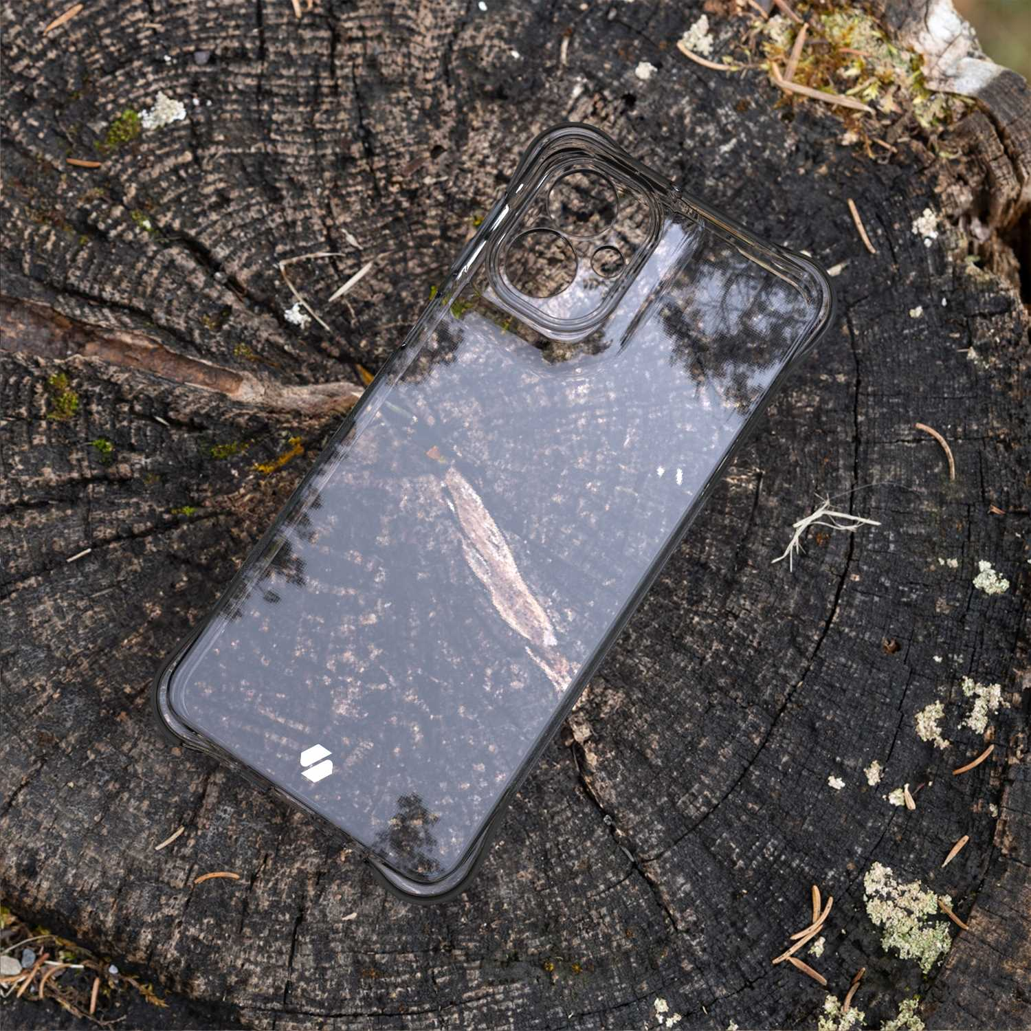 Przezroczyste etui na telefon na ciemnej drewnianej powierzchni. Etui odbija otoczenie. Drewno jest teksturowane.