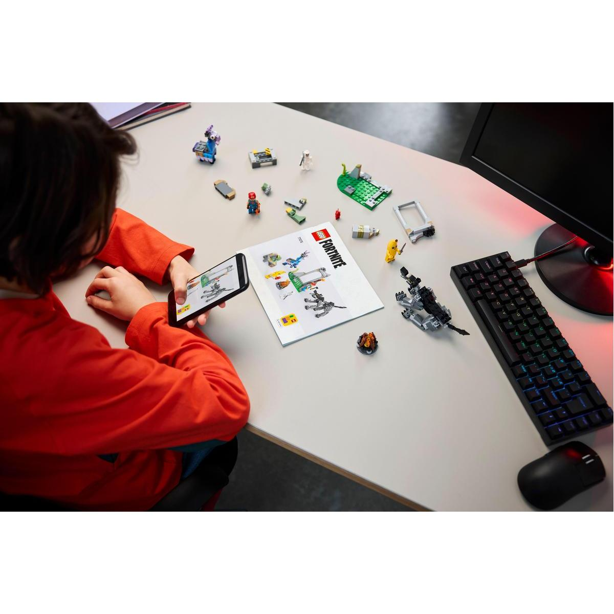 Bir çocuk, Lego talimatlarının görüntüsü olan bir telefon tutarak, bir masada Lego parçalarına bakıyor.