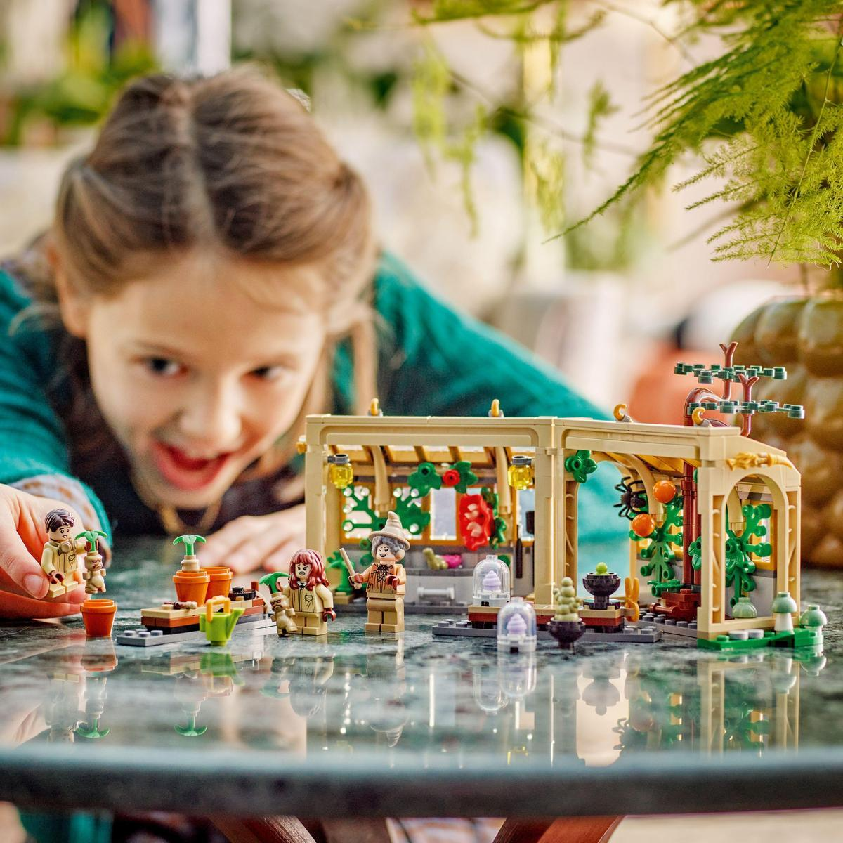 Una niña está jugando con un set de Lego con un invernadero, minifiguras y plantas.