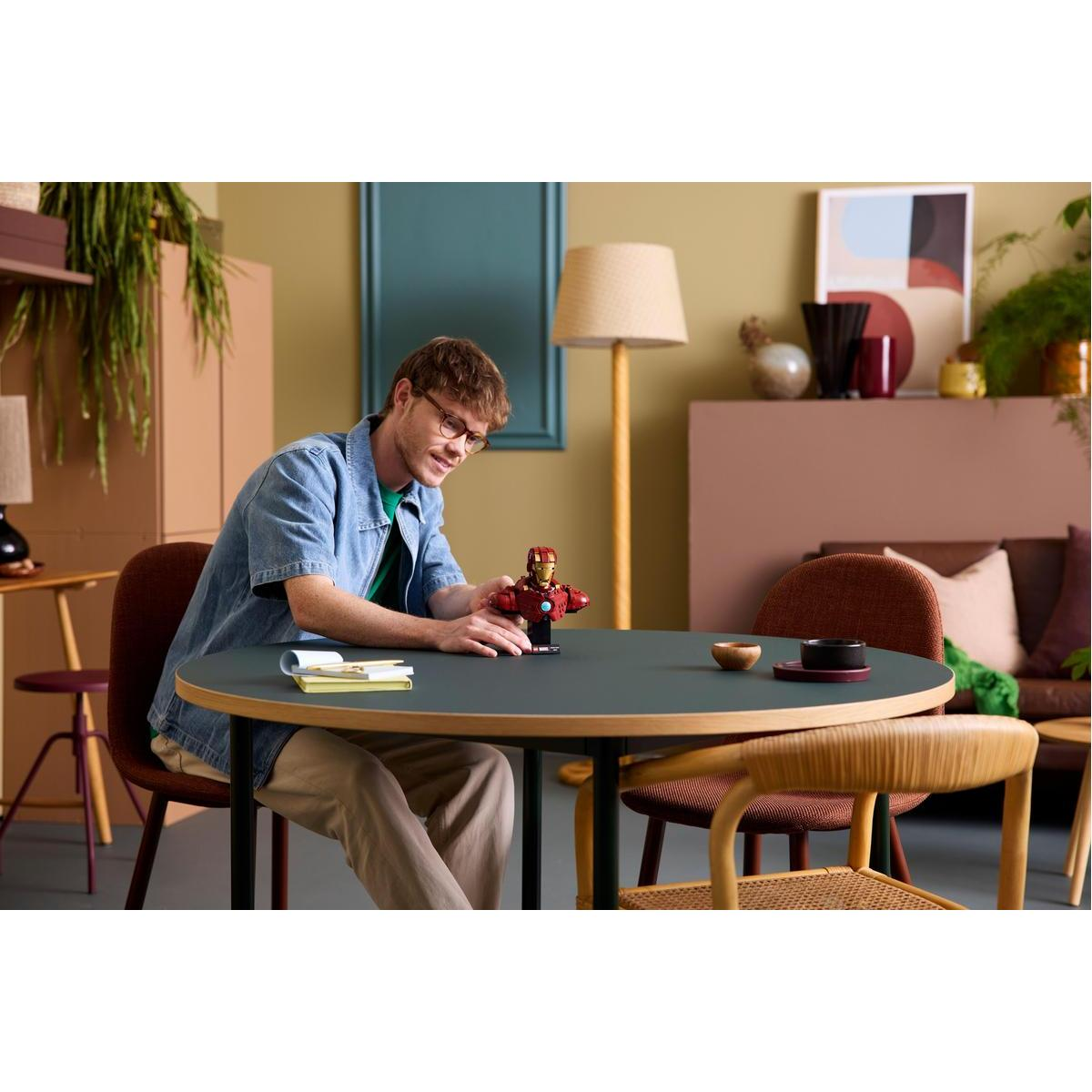 Mężczyzna siedzi przy okrągłym stole, bawiąc się figurką Lego Iron Mana.