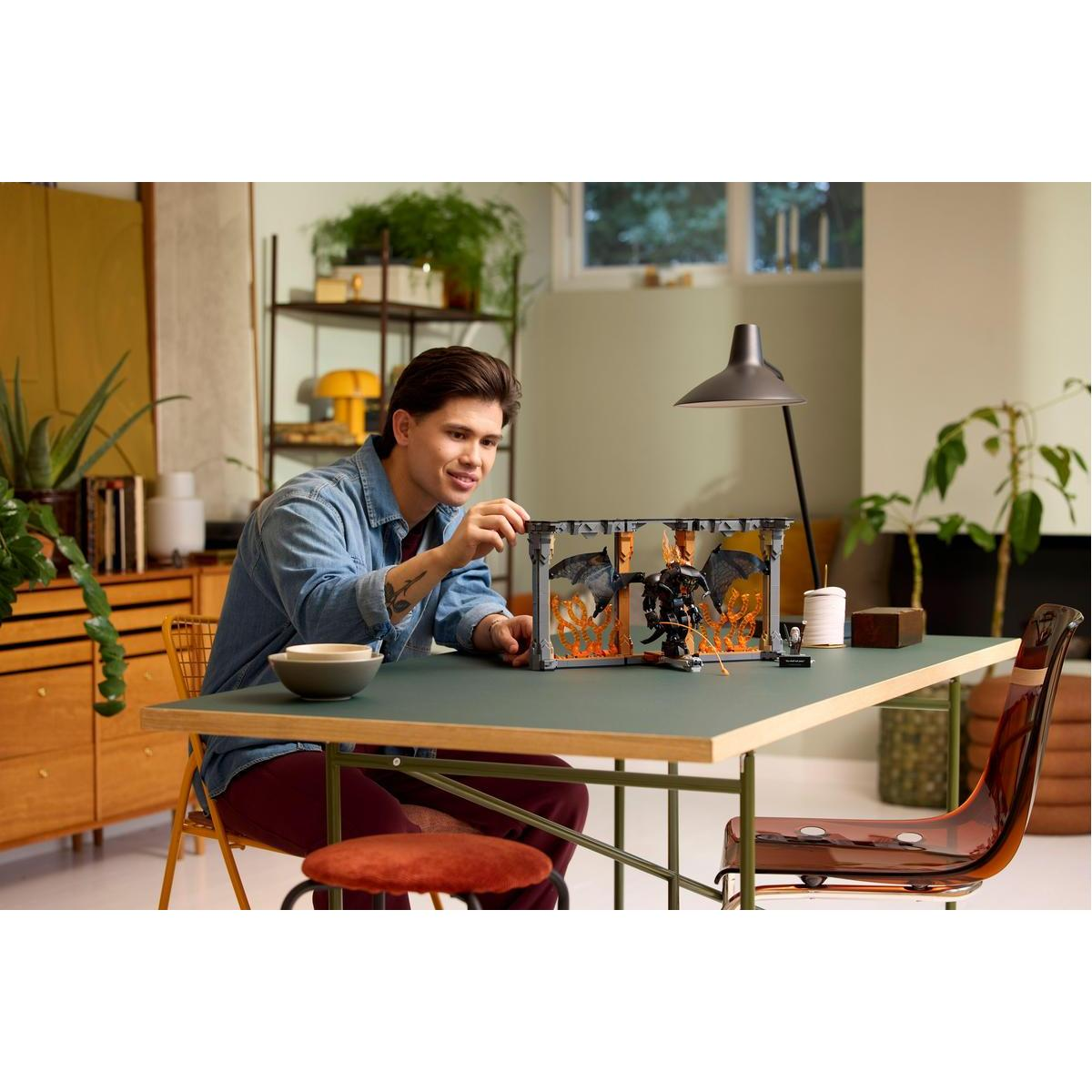 Mężczyzna siedzi przy stole, składając zestaw Lego ze smokiem i płomieniami.