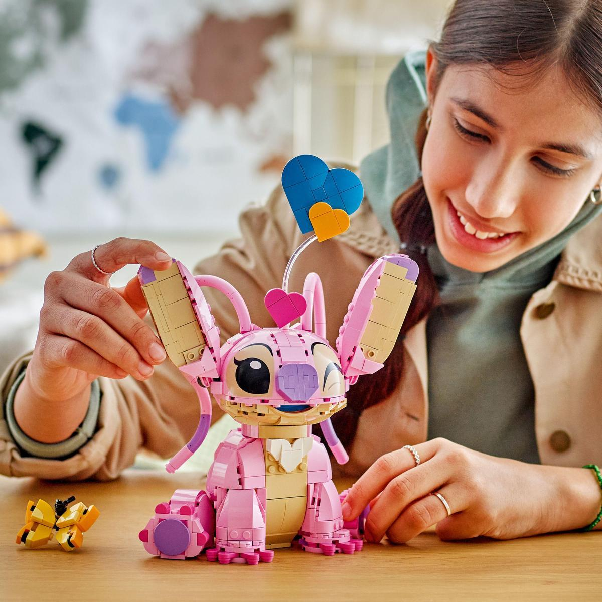 Kobieta buduje różową figurkę LEGO Stitch. Żółte i niebieskie LEGO są w pobliżu. Na górze serca.