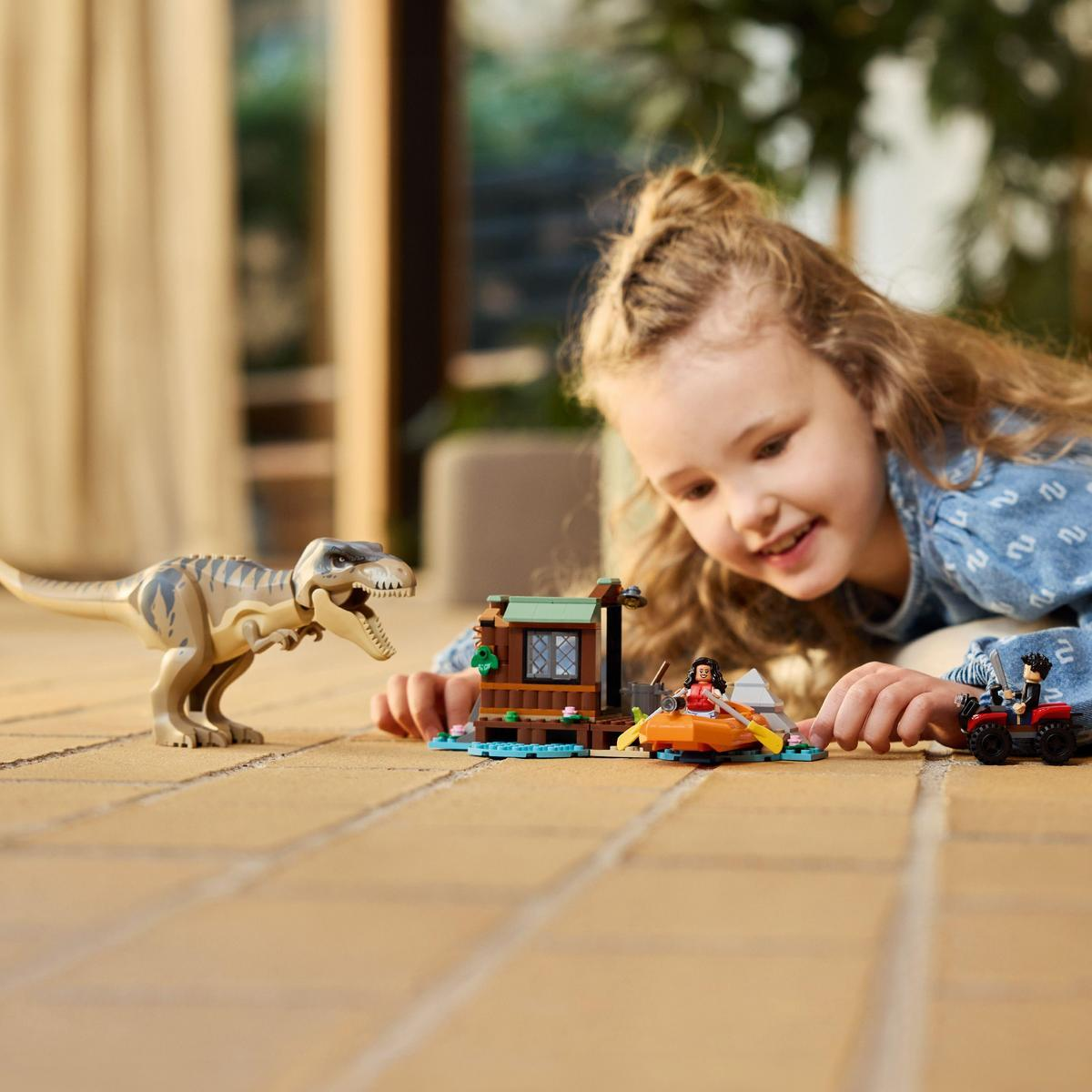 Dziecko bawi się zestawem LEGO Jurassic Park. Dinozaur stoi naprzeciwko łodzi i budynku.
