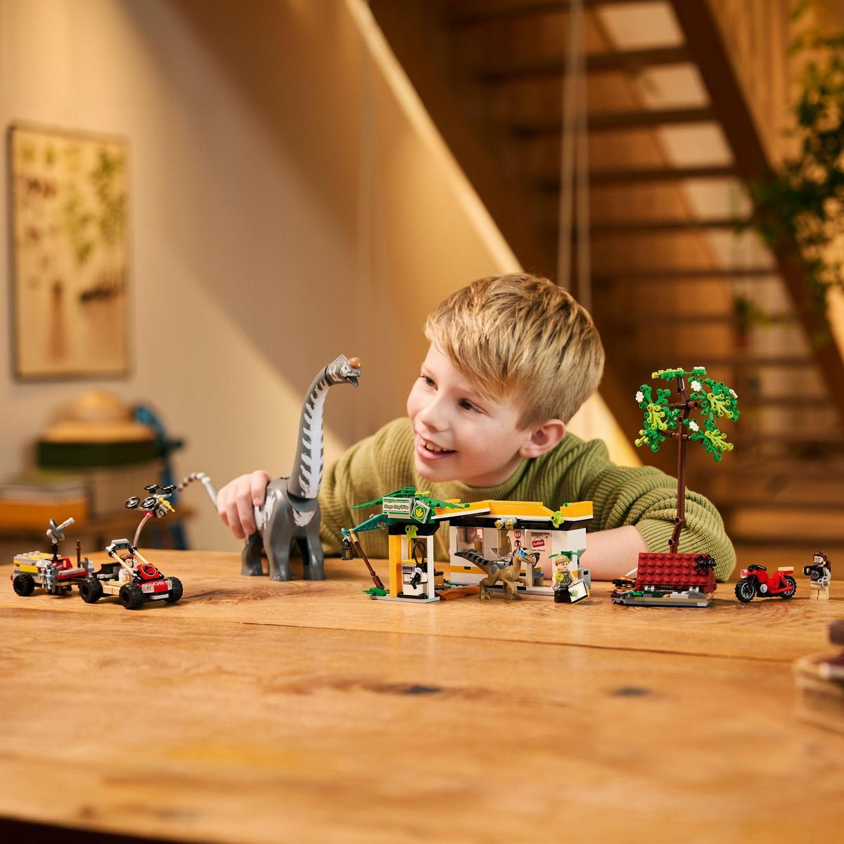 Dziecko bawi się zestawem Lego z dinozaurami, samochodem i konstrukcją na stole.