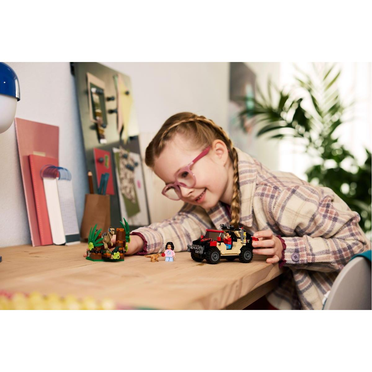 Dziecko bawi się zestawem Lego z samochodem, figurkami i sceną z dinozaurami.