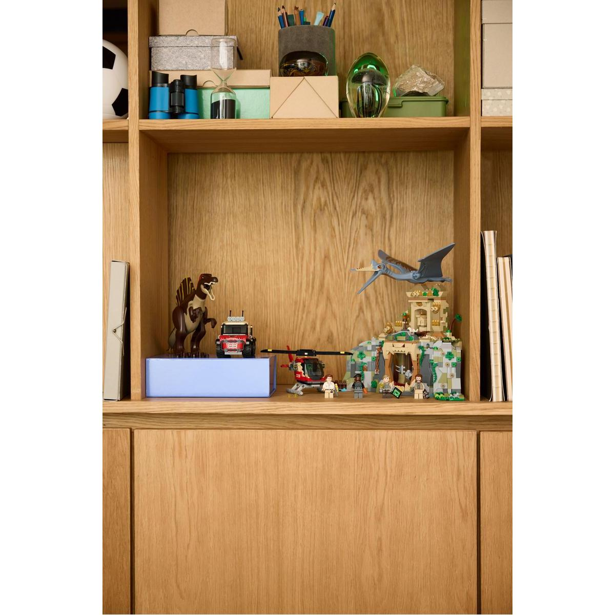 Drewniana półka prezentuje zestawy Lego z dinozaurem, ciężarówką i świątynią. Książki po obu stronach.
