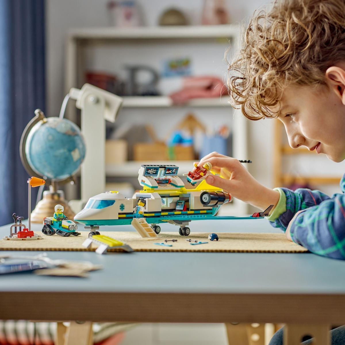 Chłopiec bawi się zestawem Lego z samolotem i innymi akcesoriami na stole. Po lewej stronie globus.