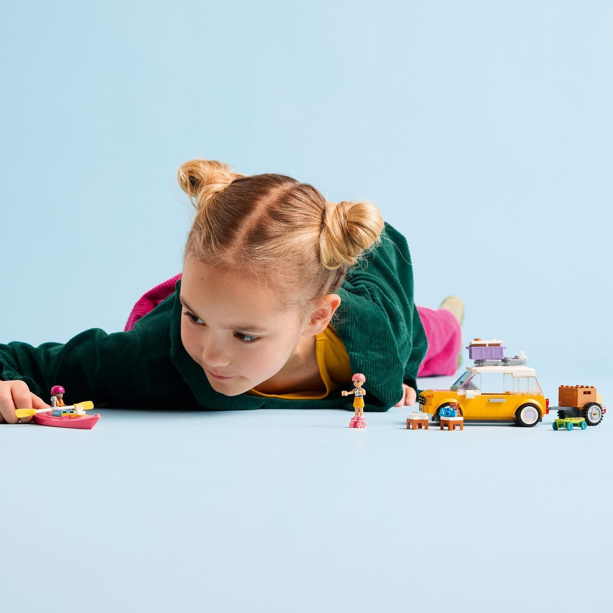Dziewczynka bawi się zestawem Lego Friends. Samochód, przyczepa i figurki znajdują się na niebieskiej powierzchni.