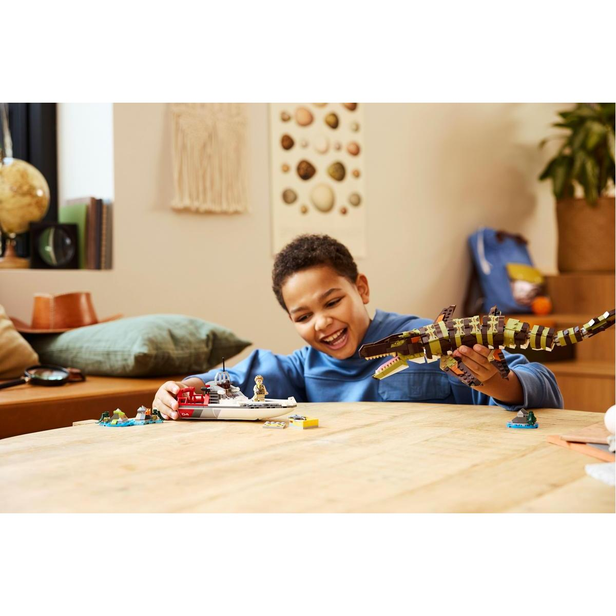 Chłopiec bawiący się zabawką Lego w postaci łodzi i dużym dinozaurem Lego na drewnianym stole.