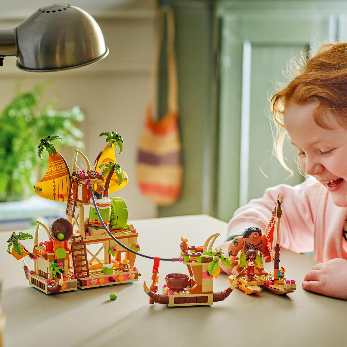 Dziewczyna bawiąca się zestawem Lego Moana, przedstawiającym łódź Moany i inne tropikalne struktury.