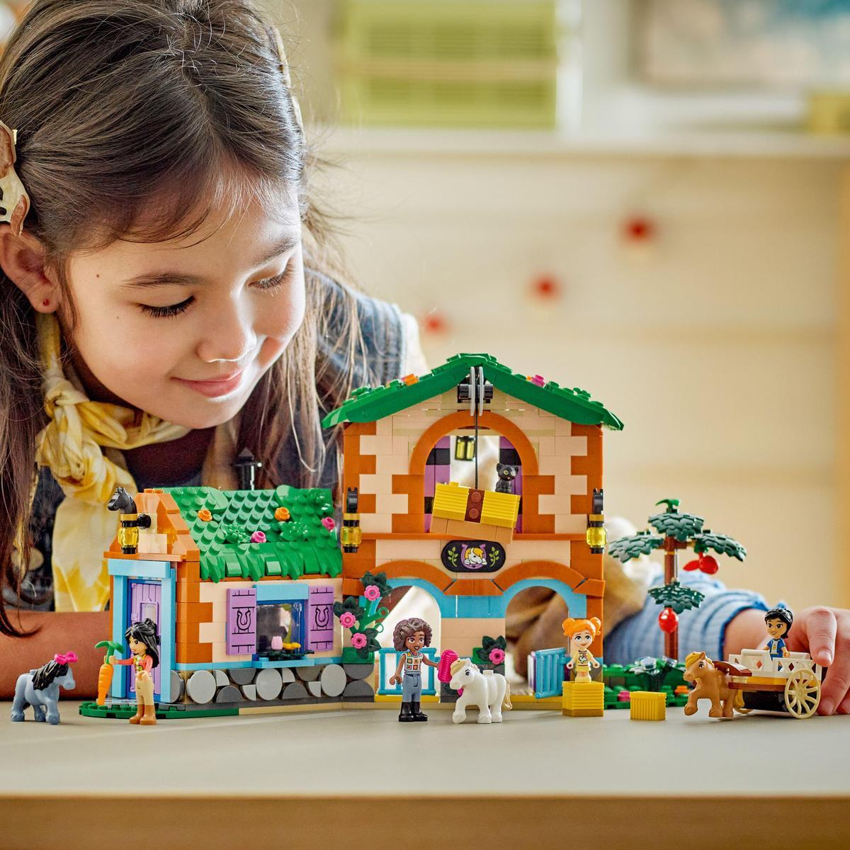 Bir kız, bir ev, figürler ve atları tasvir eden bir Lego setine bakıyor.
