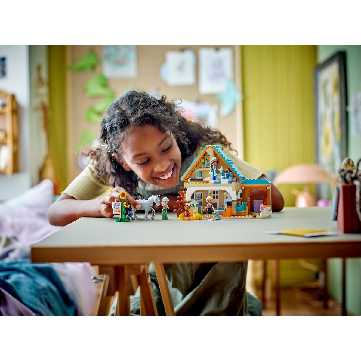 Une fille sourit devant un jeu Lego. Il représente une maison avec des personnages et un cheval.