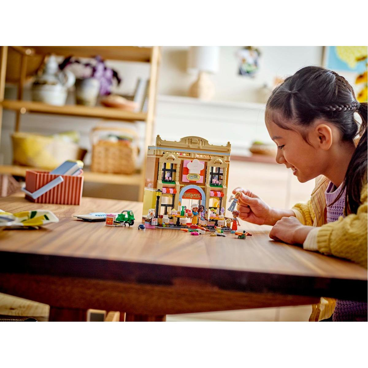 Dziewczynka bawi się zestawem restauracji Lego. Uśmiecha się i patrzy na zestaw na drewnianym stole.