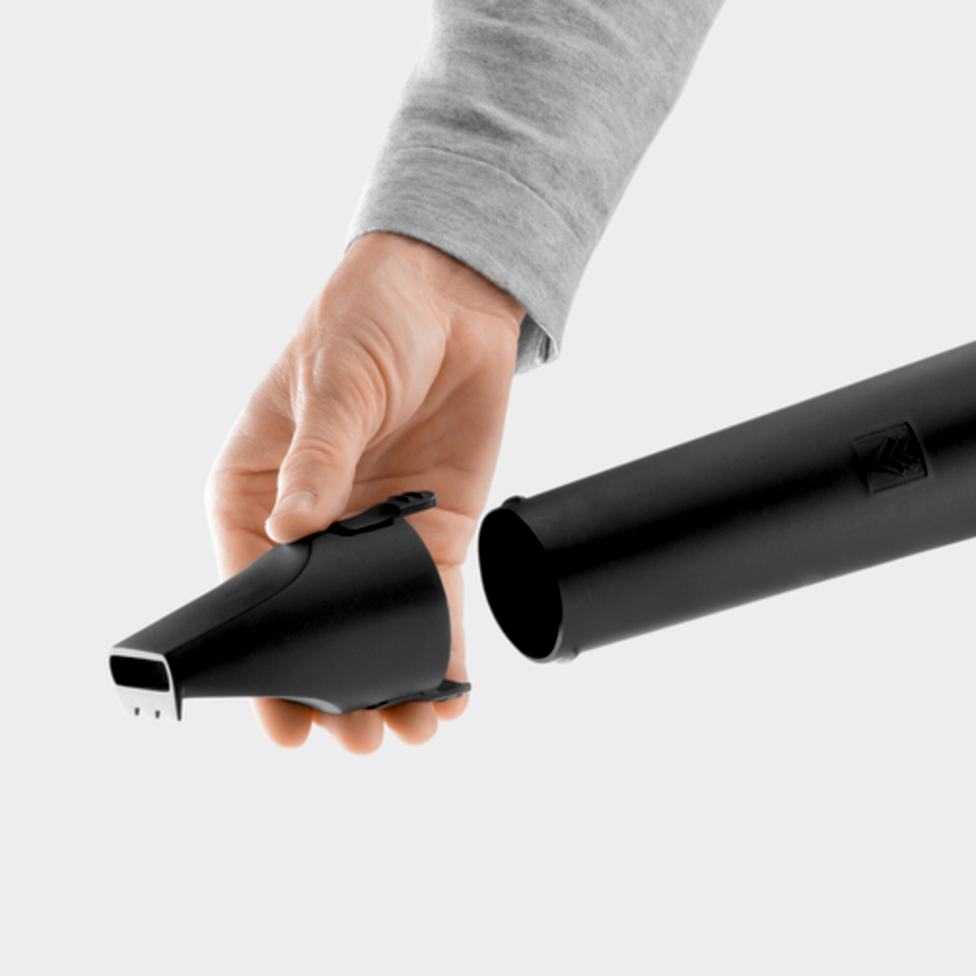 Ręka mocuje dyszę do czarnej dmuchawy do liści. Białe tło.